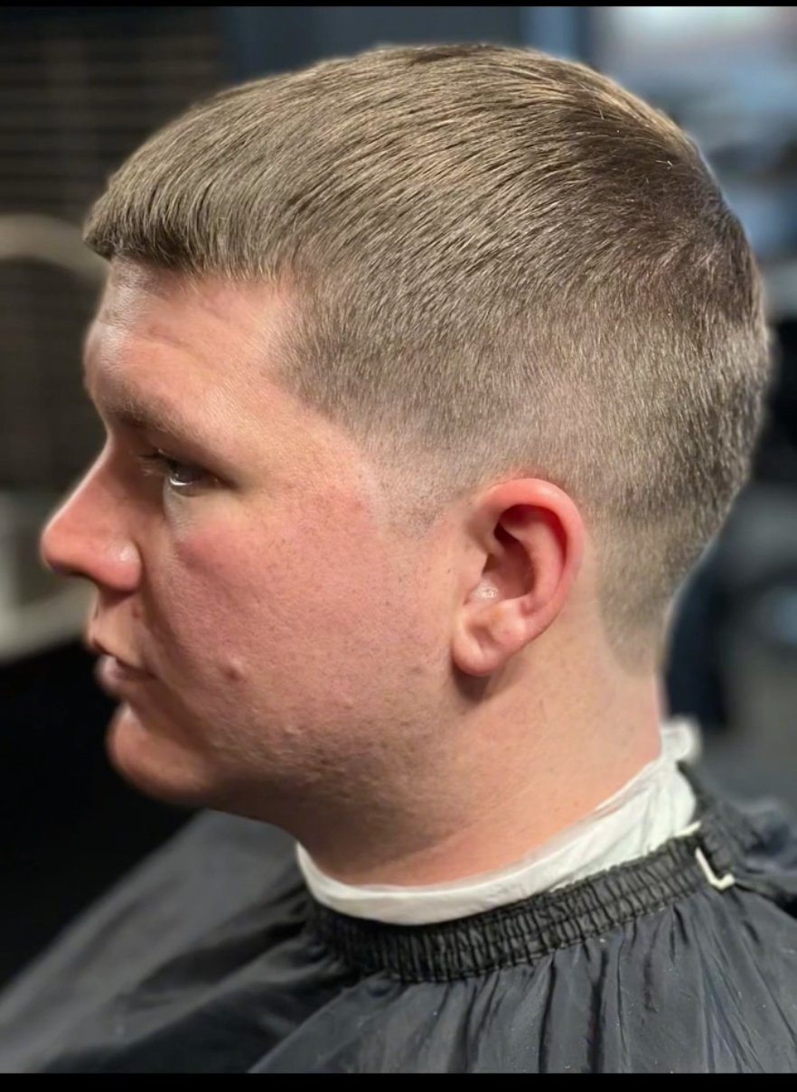 Close-up side view of a man with a fresh short haircut, fade style, and blond hair, sitting in a barber chair.