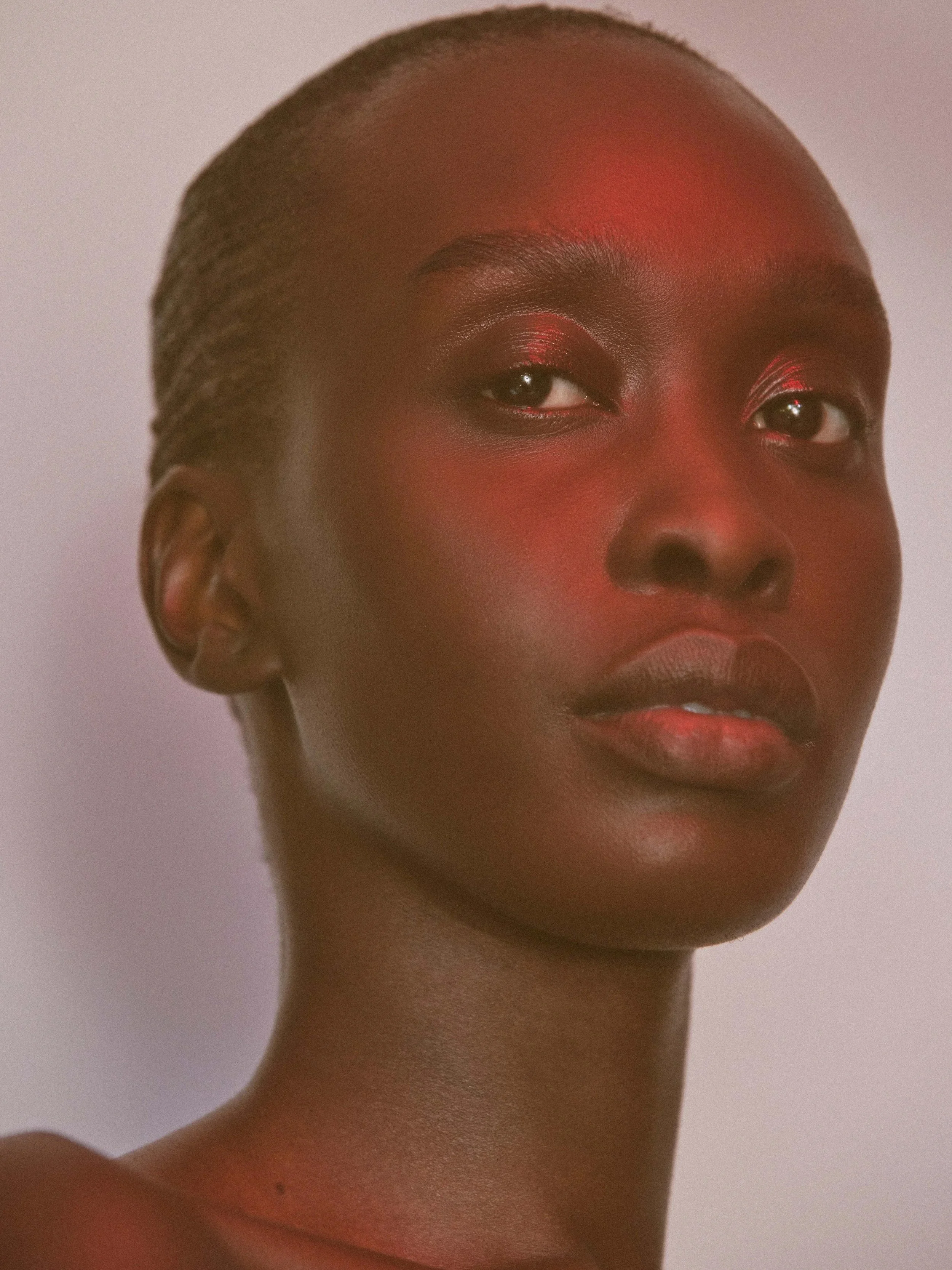 Close-up portrait of a woman with dark skin and natural hair styled in small twists, against a plain background.