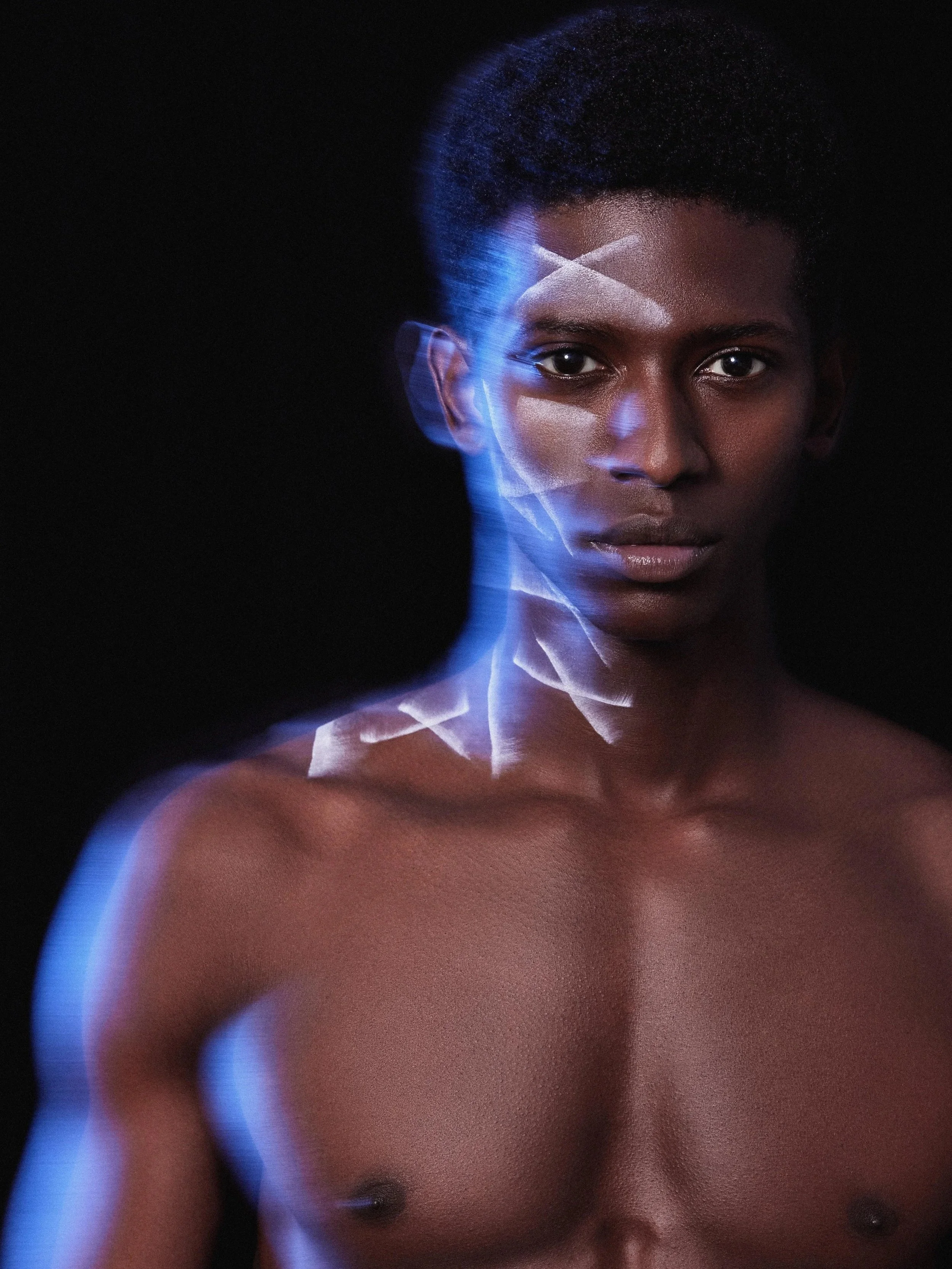 A shirtless person with dark skin and short curly hair, with a surreal glow and light trails around their face and shoulder against a black background.
