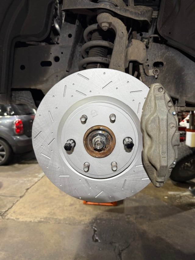 Close-up of a car brake rotor with caliper, mounted on a vehicle in a garage.