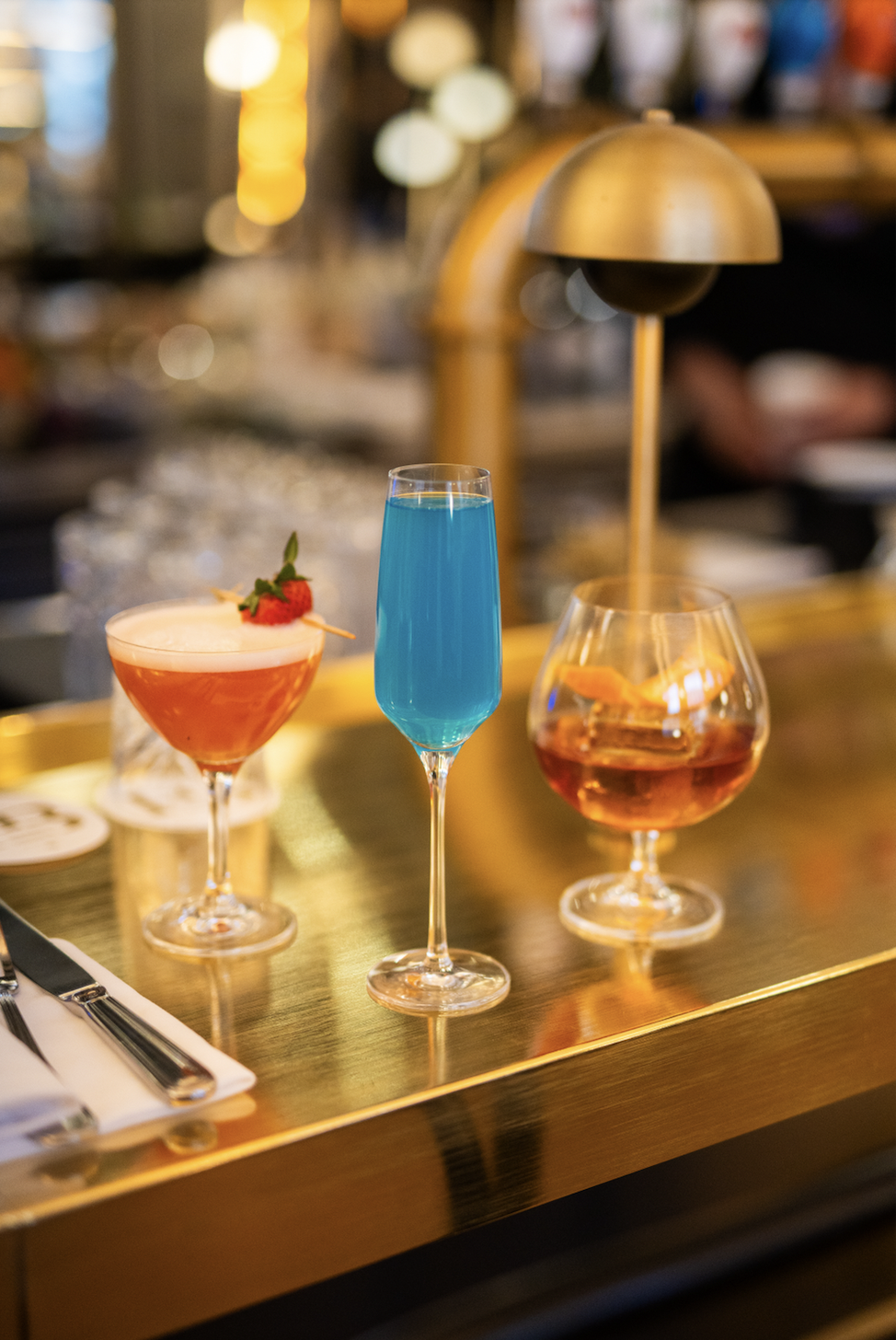 Three colorful cocktails on a bar counter with blurred background.