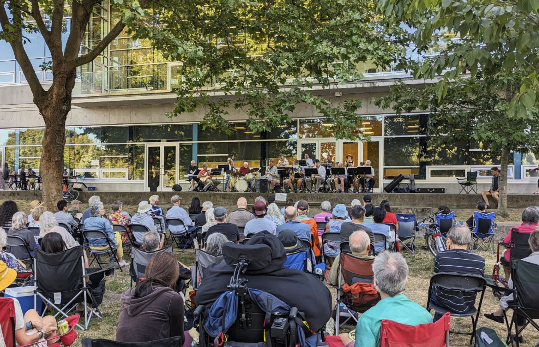 People are seated and enjoying the Summer Outdoor Concert Series at the Trout Lake Community Centre