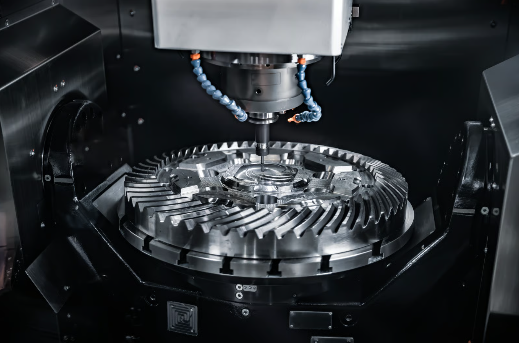 Industrial machine with a rotating circular metal component being machined, with robotic blue flexible hoses above.