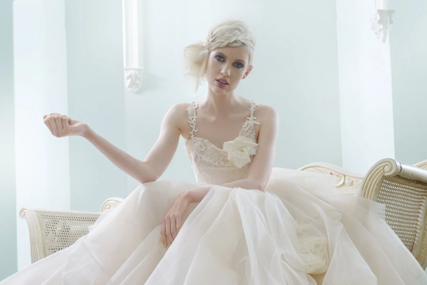 Young woman in a fancy cream-colored dress sitting on a vintage-style sofa in a softly lit room.