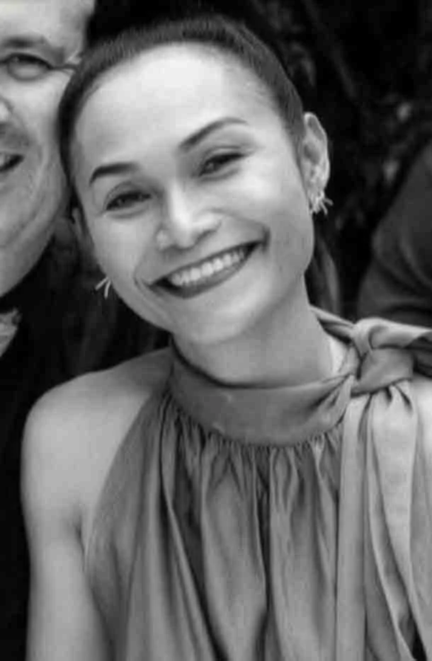Smiling woman with her hair in a bun, wearing earrings and a sleeveless, high-neck dress.