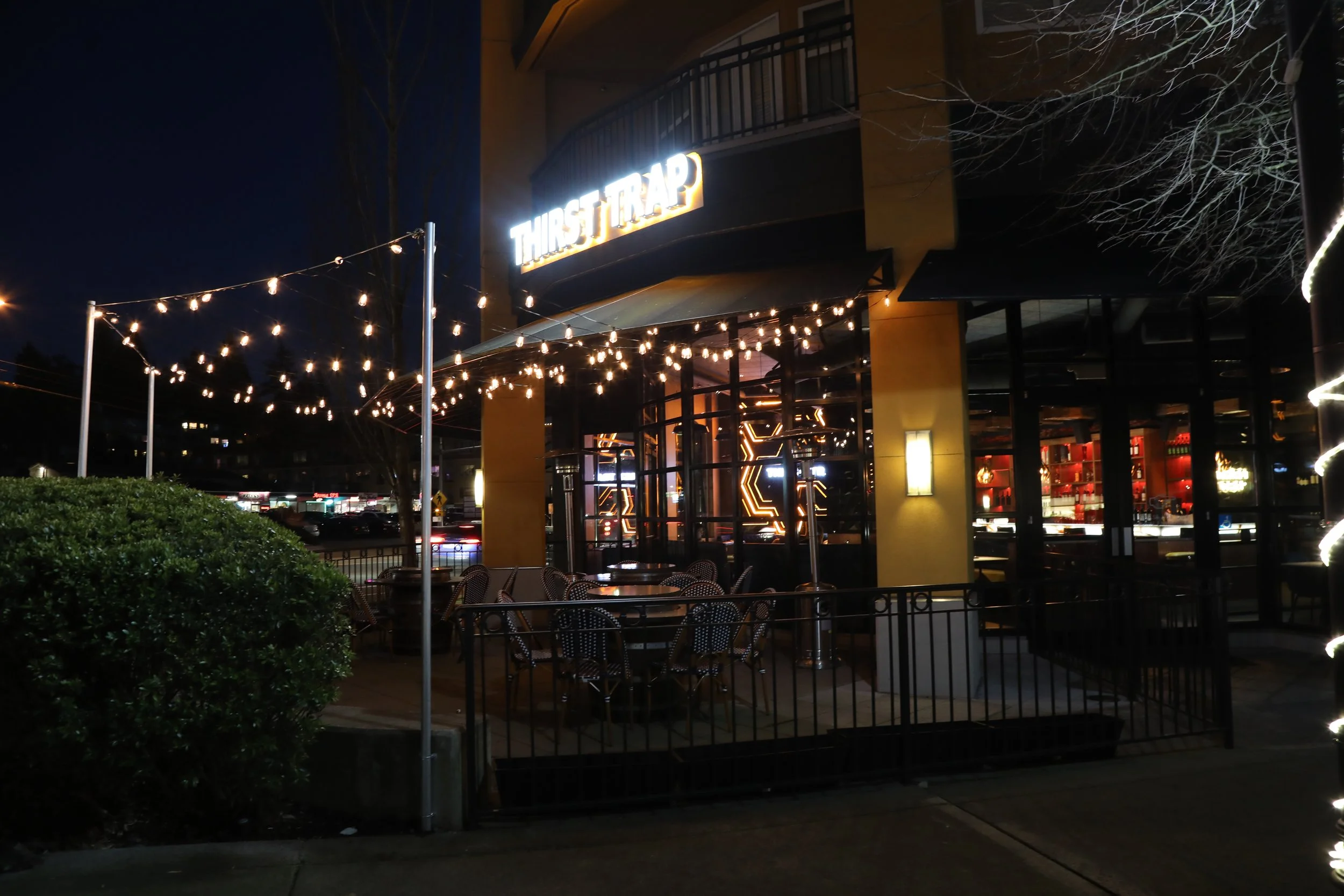 Outdoor seating area of a restaurant named Thirst Trap with decorative string lights at night.