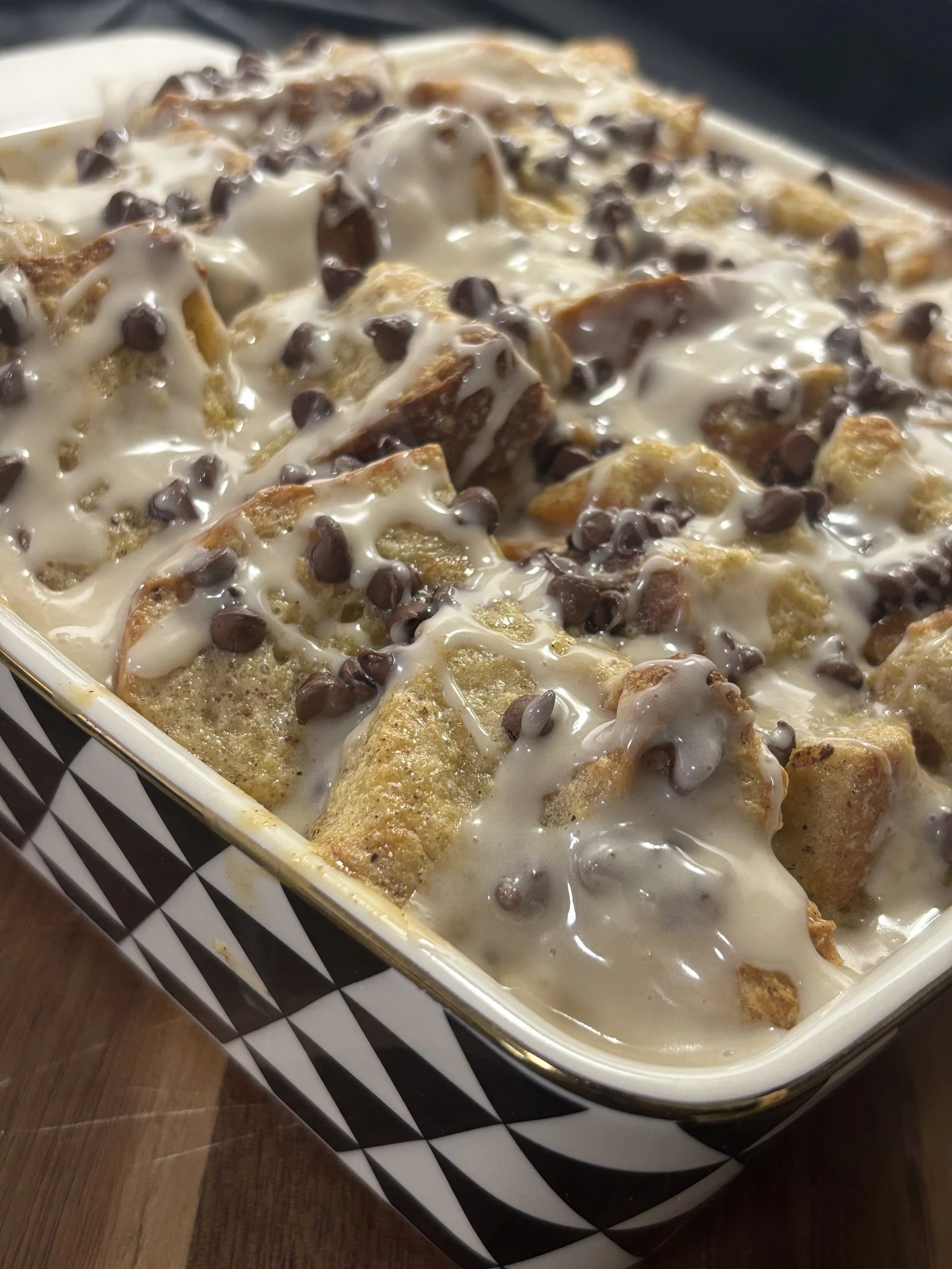 A baking dish filled with bread covered in creamy sauce, chocolate chips, and topped with chopped nuts.