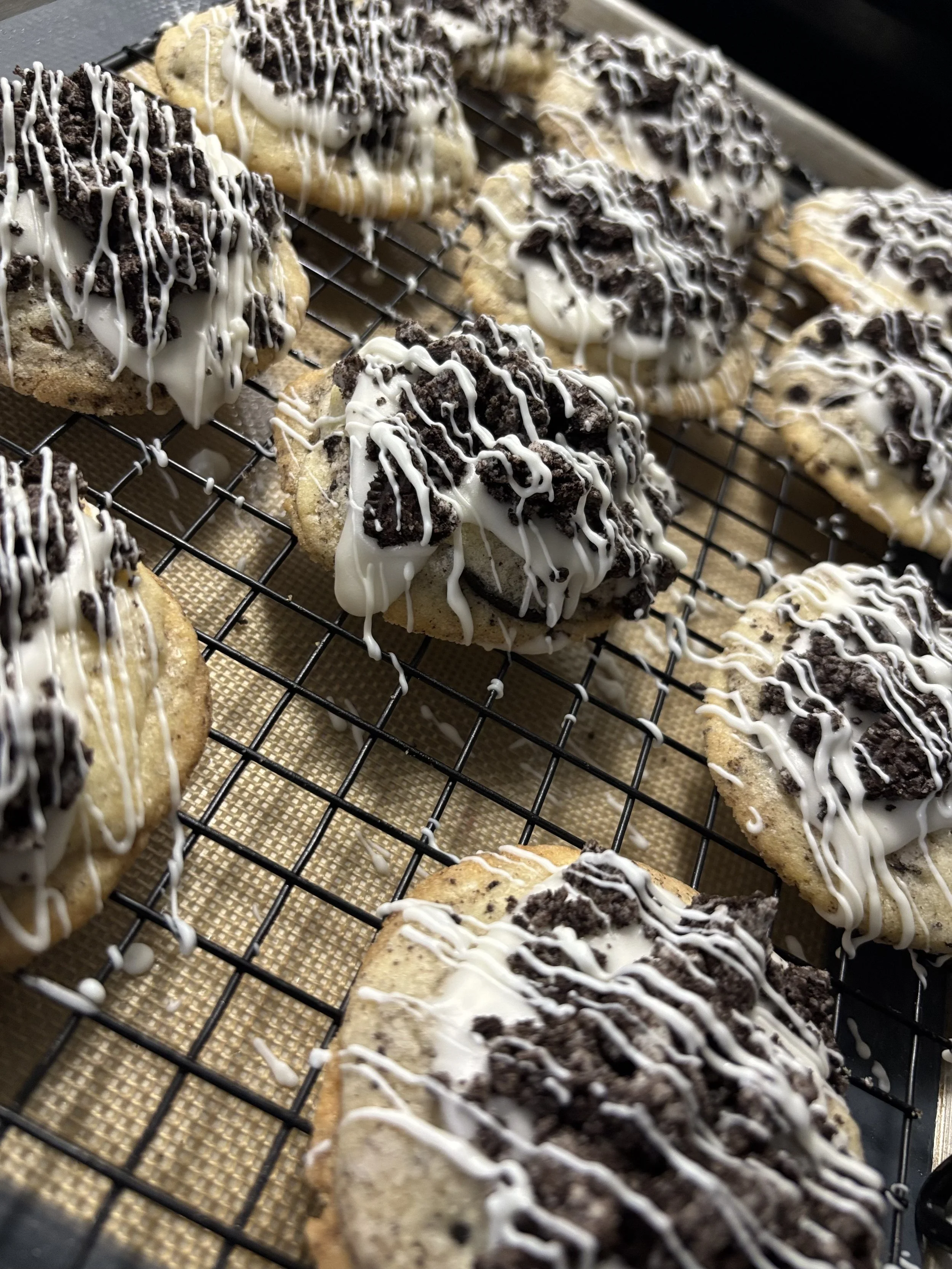 Cookies with white icing and crushed Oreo cookies on top, drizzled with white icing, resting on cooling rack.