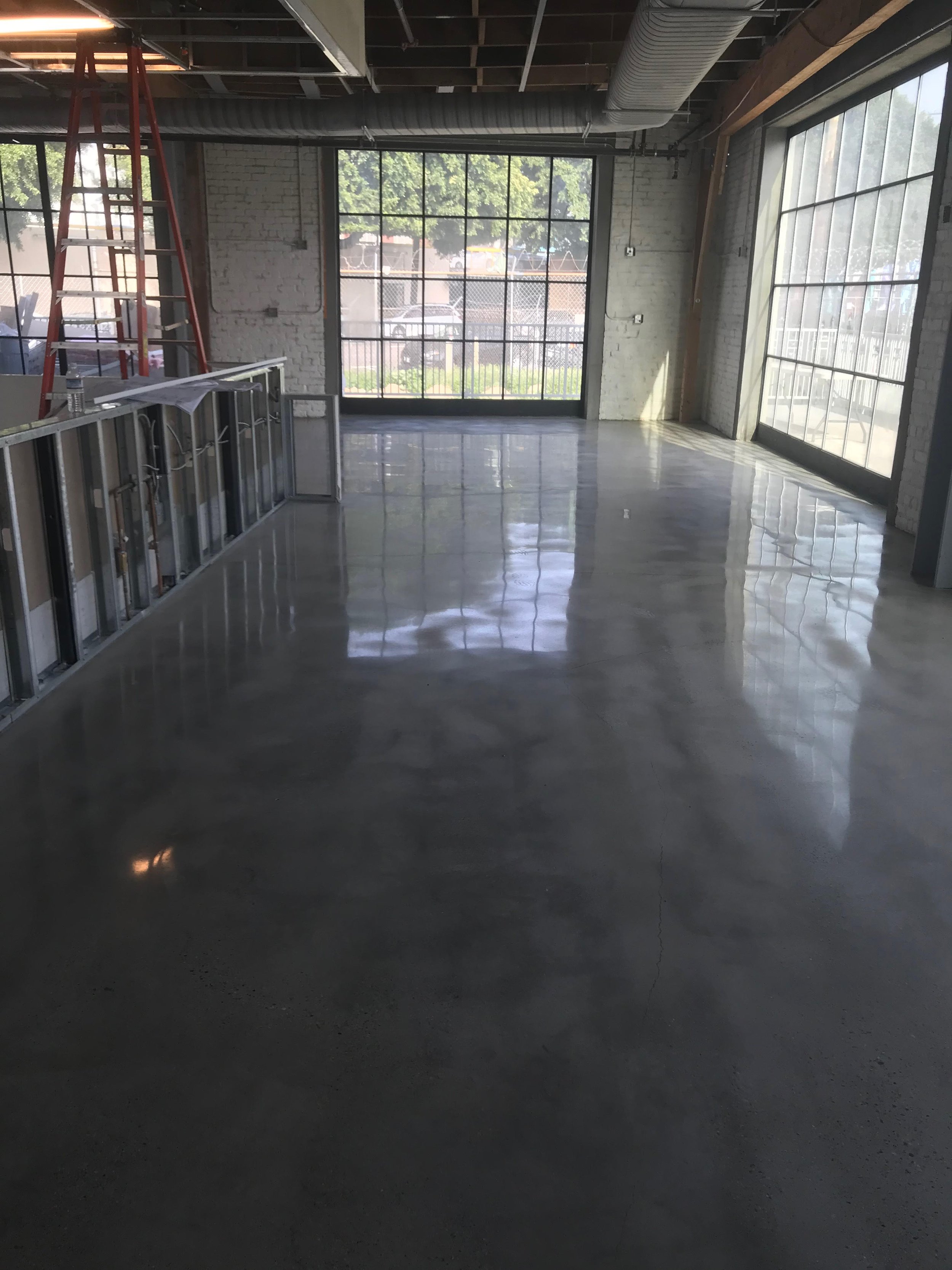 Empty commercial interior space with large windows, polished concrete floors, unfinished walls, and a ladder.
