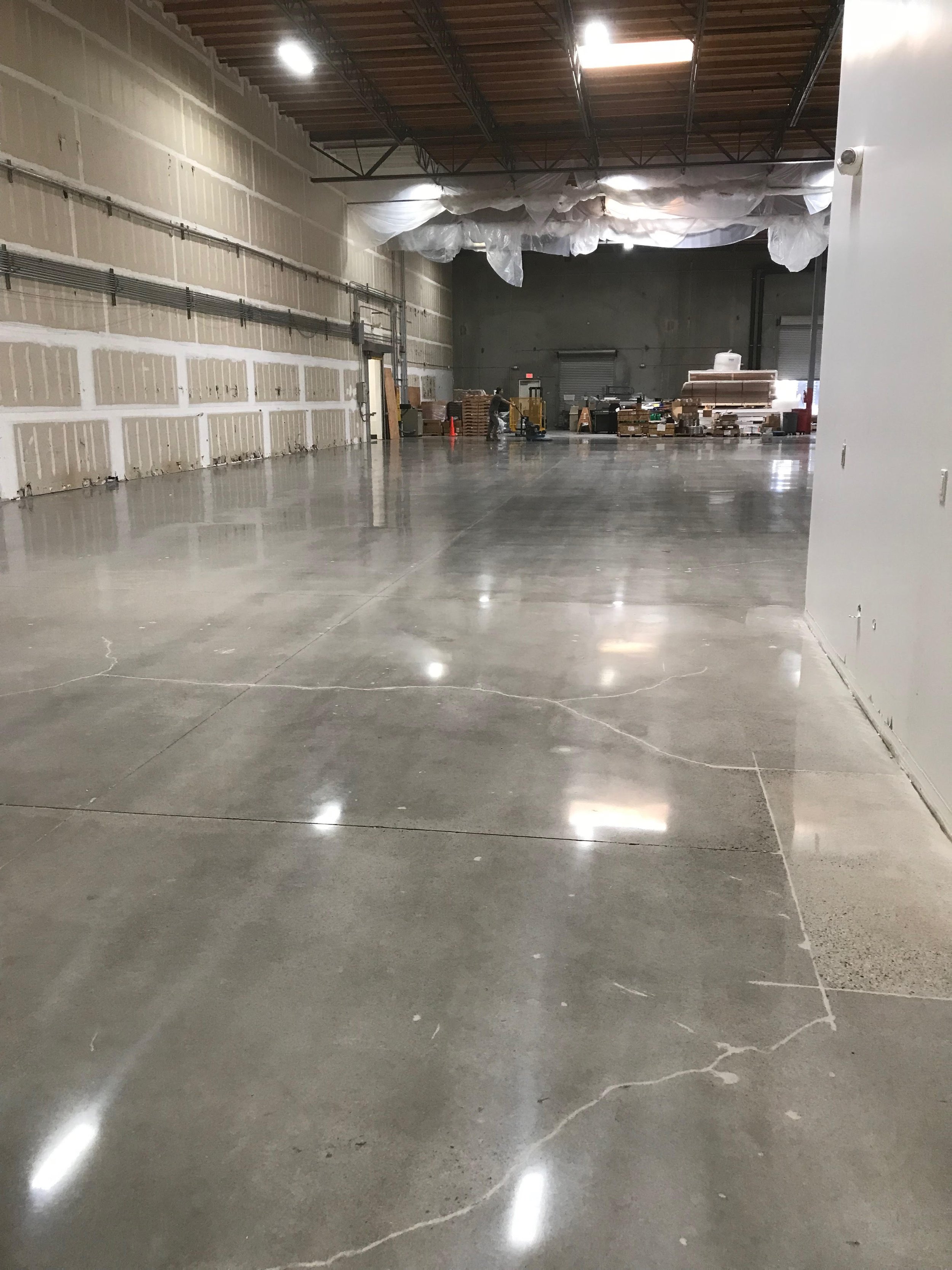 Empty warehouse with polished concrete floors, construction materials, and equipment in the background.