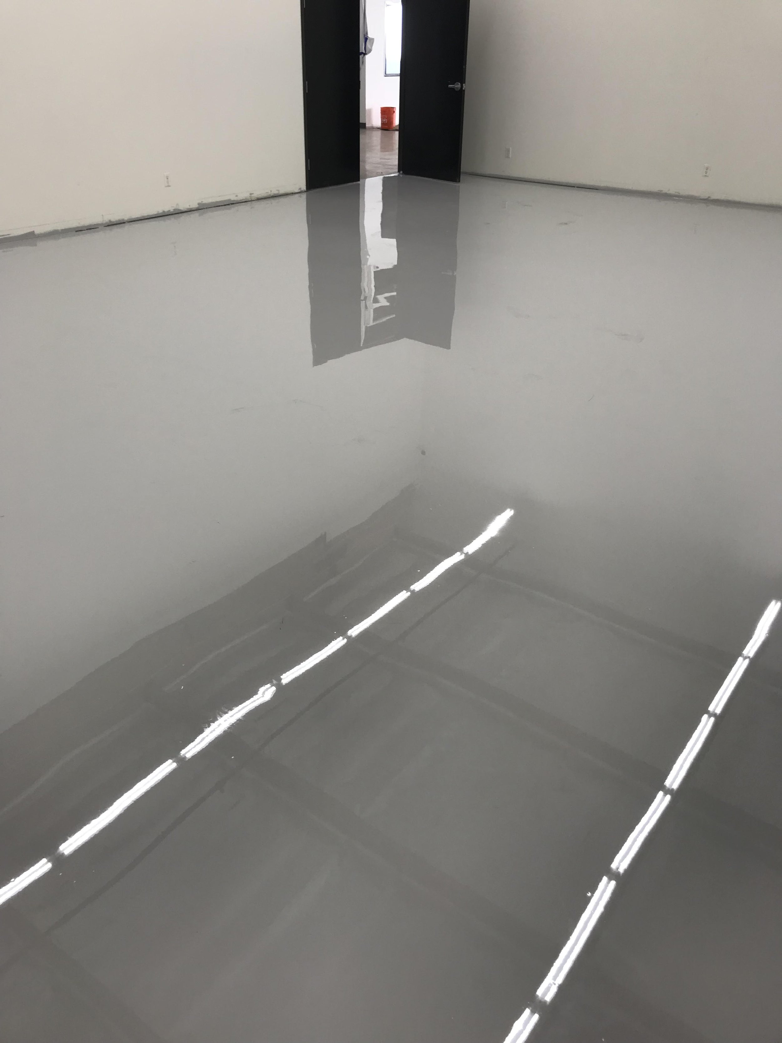 Empty room with a shiny, reflective gray epoxy floor and an open door leading to another room with a bucket visible.