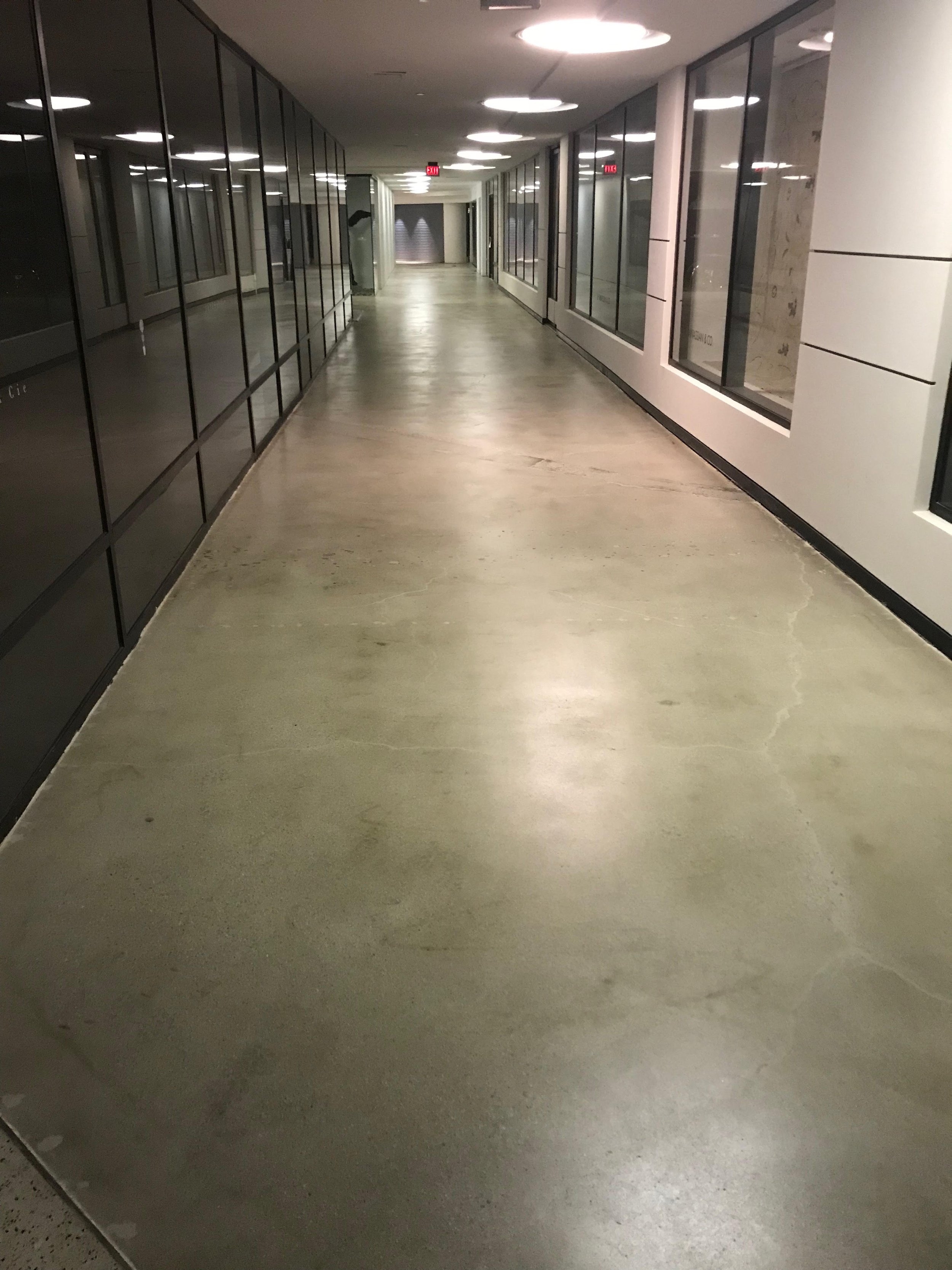 Empty indoor hallway with glass windows on both sides, overhead circular lighting, and a concrete floor.