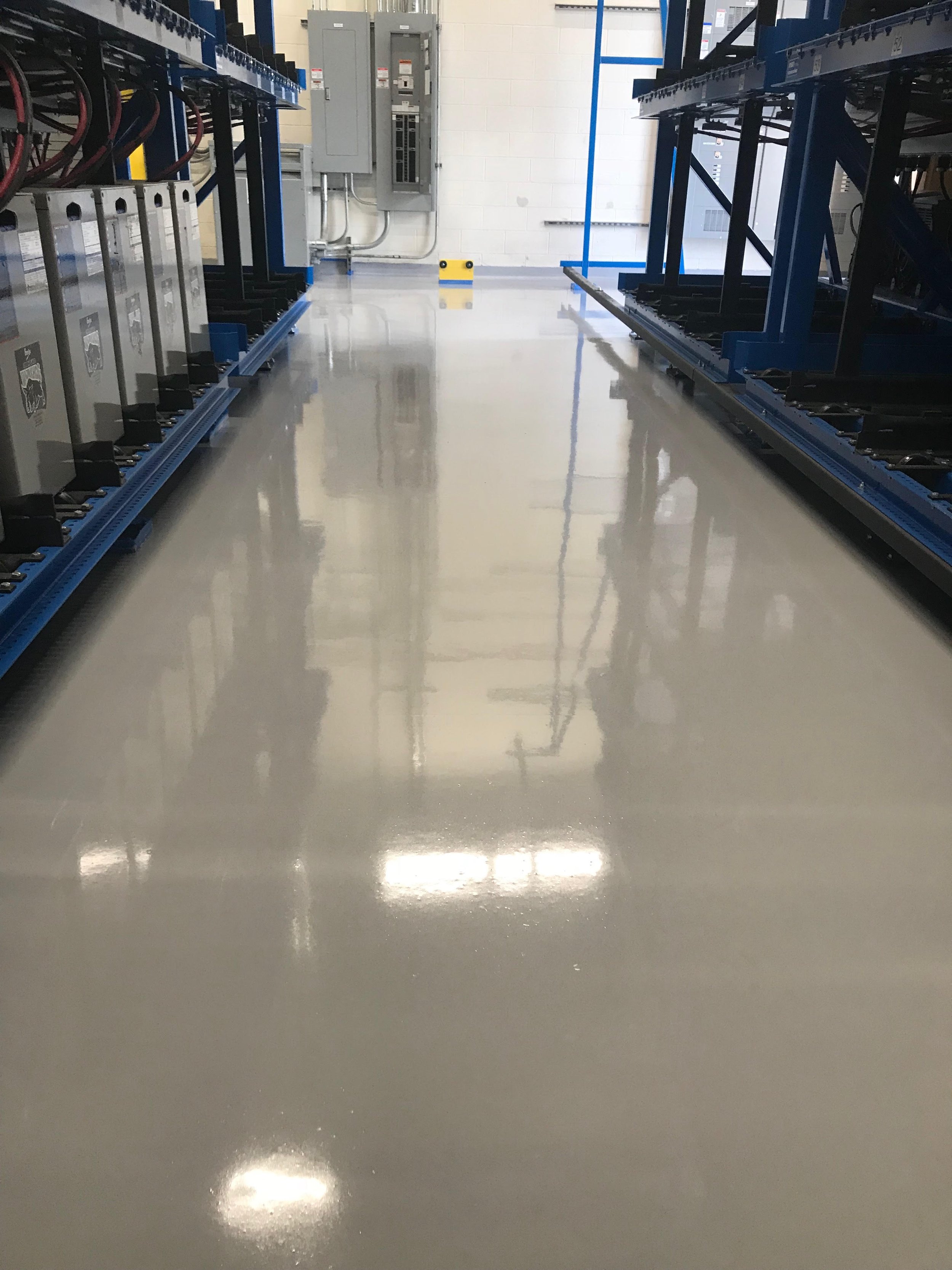Clean, shiny factory or data center floor with blue shelving and electrical panels on the wall.
