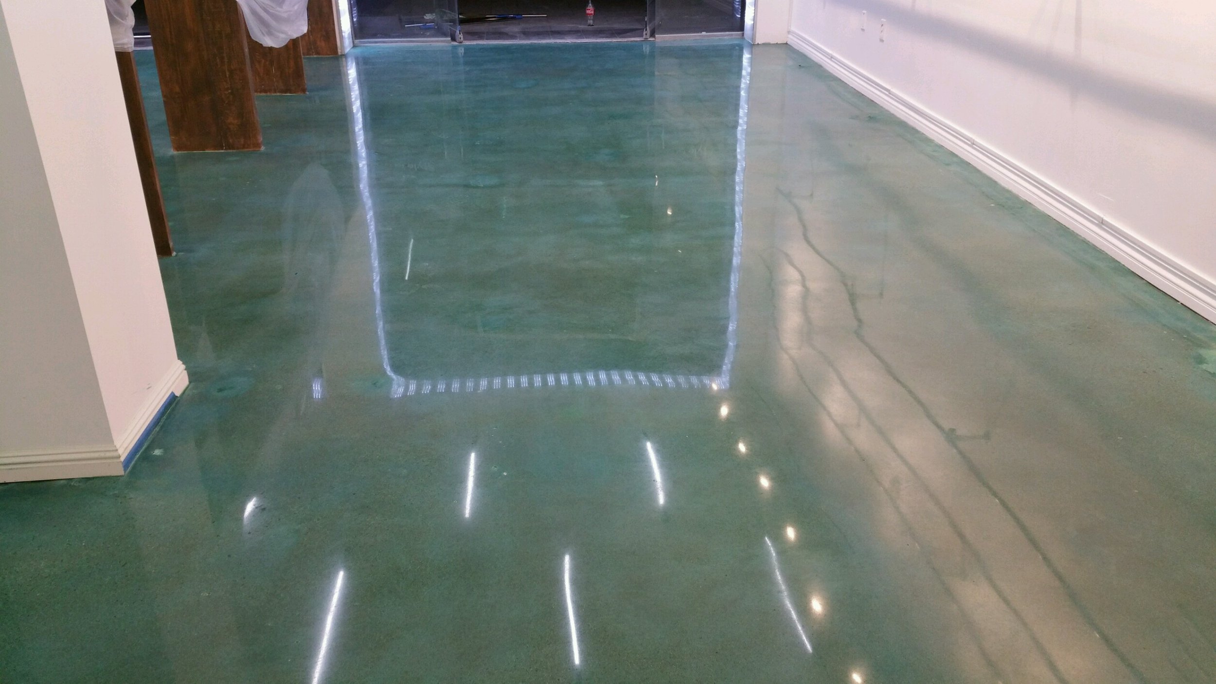 Polished green concrete floor with reflections of ceiling lights and part of a doorway.