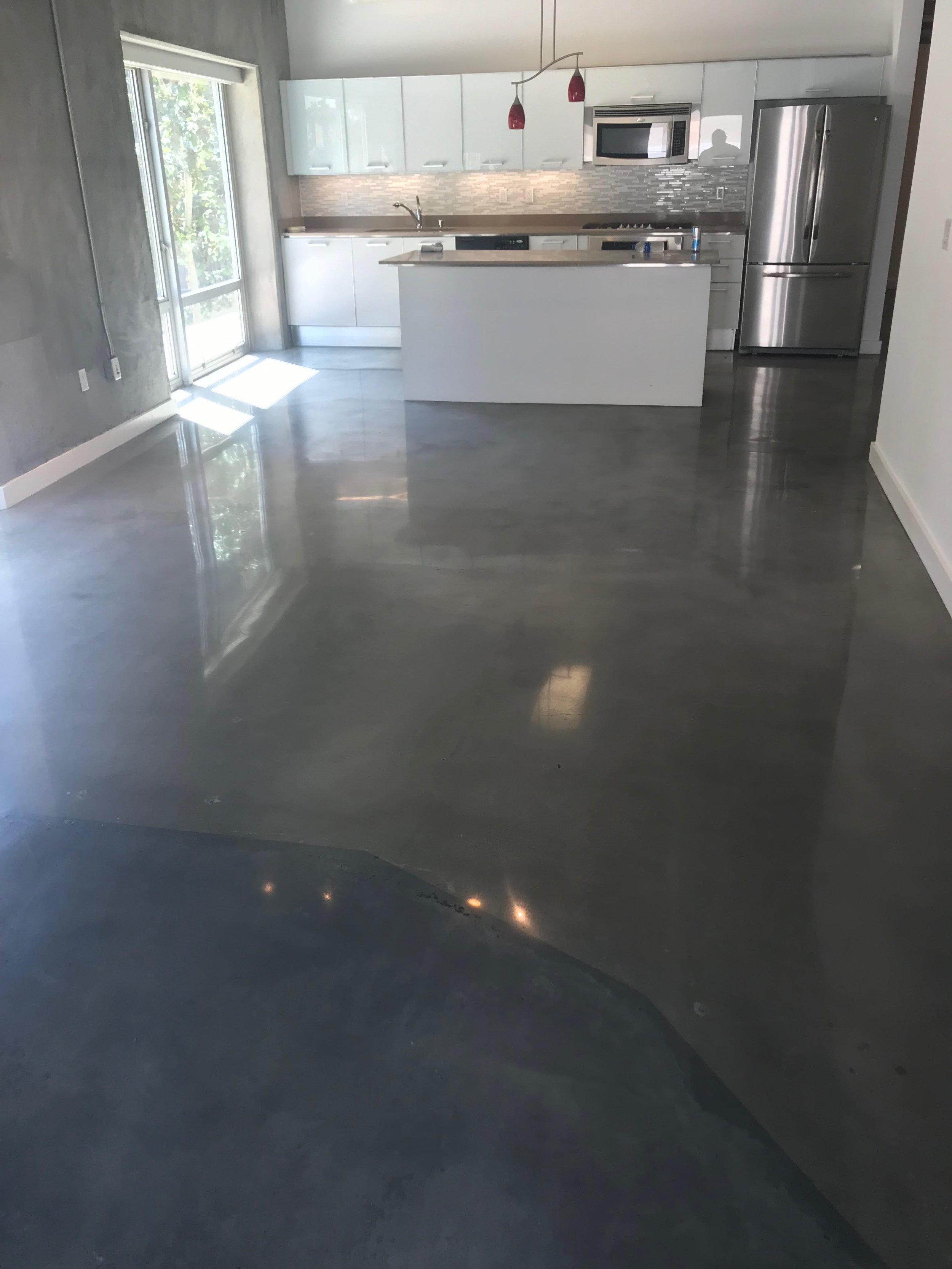 Modern kitchen with white cabinets, stainless steel refrigerator, microwave, and stove, open layout with polished concrete floors, and a sliding glass door letting in natural light.