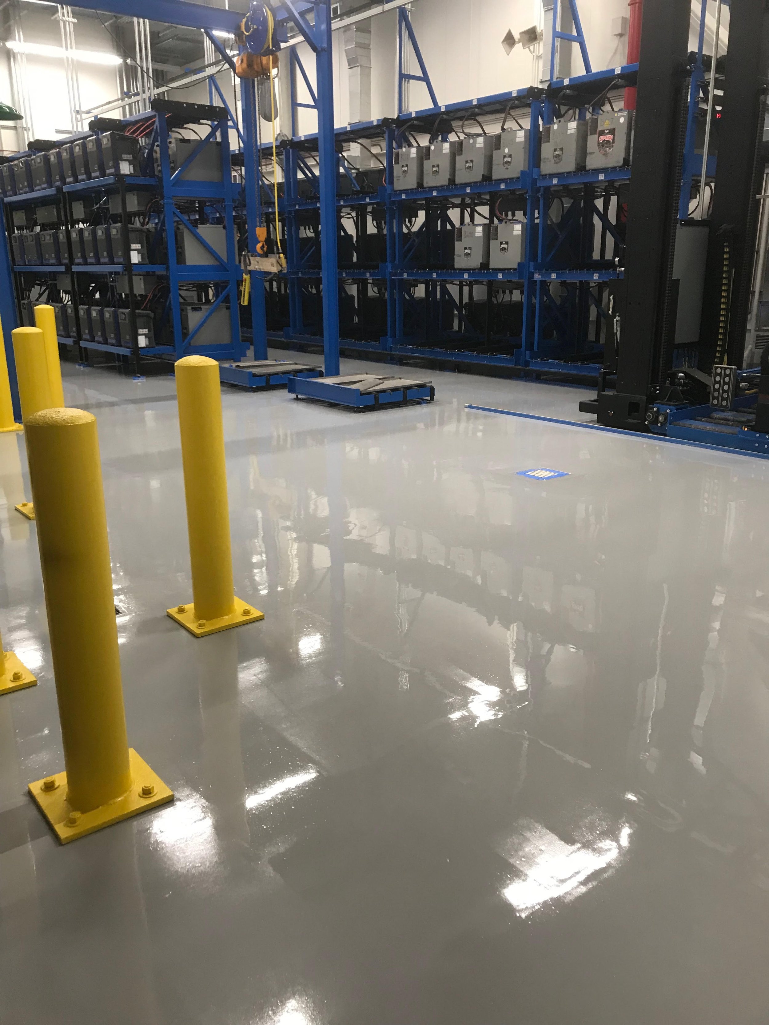Industrial data center with blue server racks and yellow safety bollards on a polished gray floor.