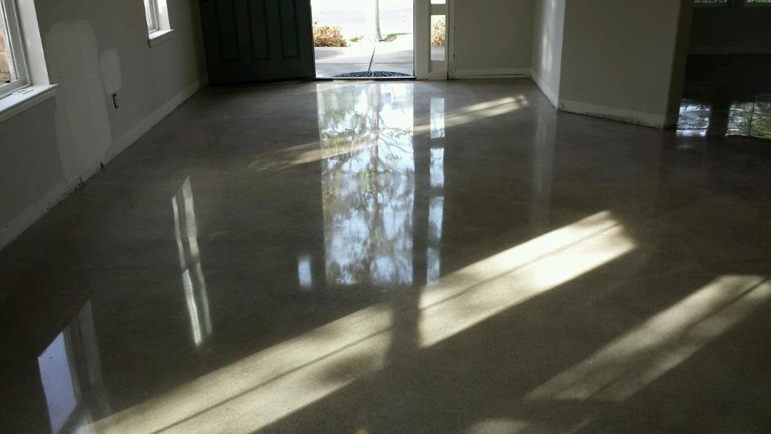 Empty room with a bright polished concrete floor, reflecting sunlight streaming through windows and glass door.