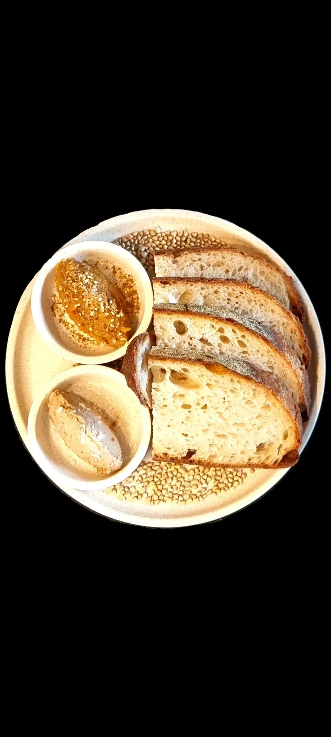 Plate with sliced bread, two bowls of spreads, and sesame seeds