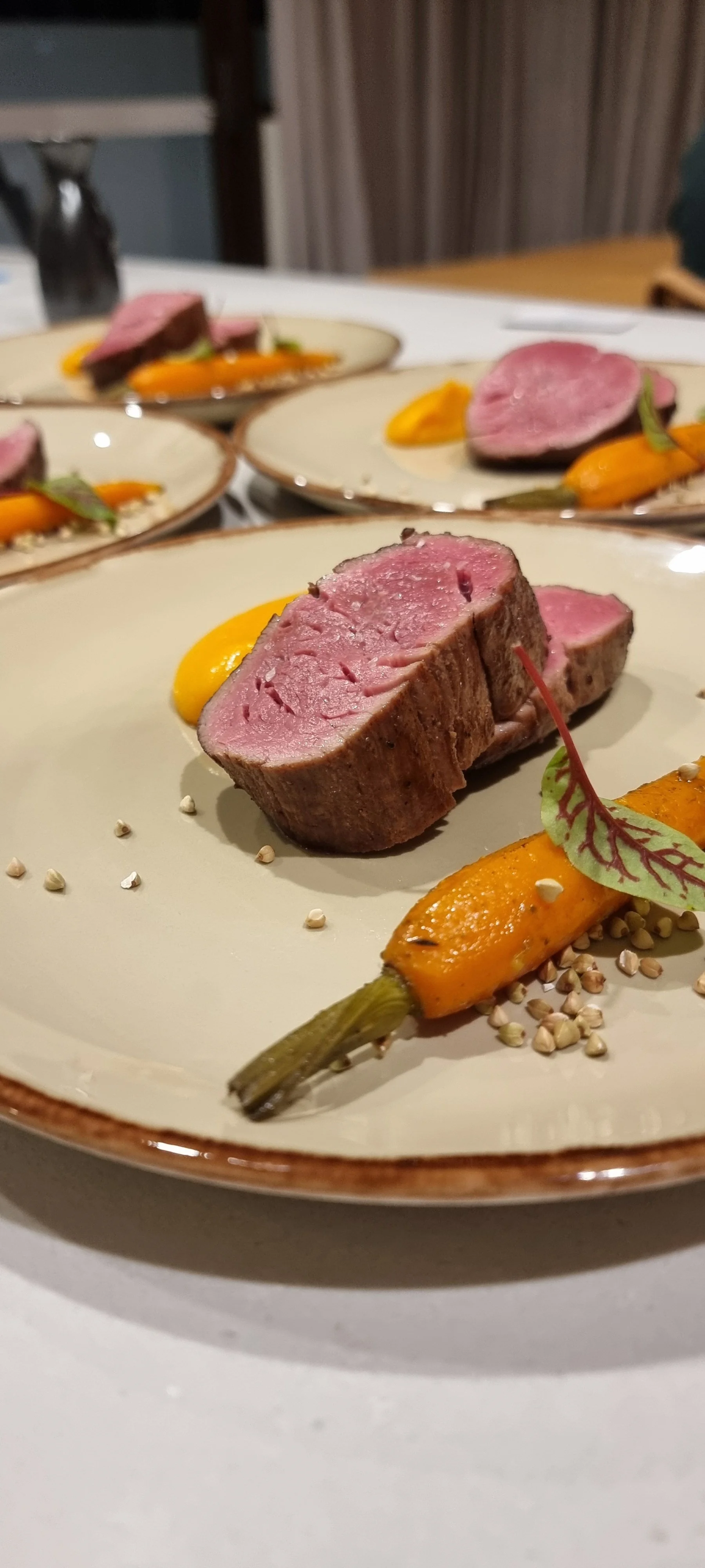 Gourmet dish with sliced meat, orange puree, roasted carrot, and garnish on plate.