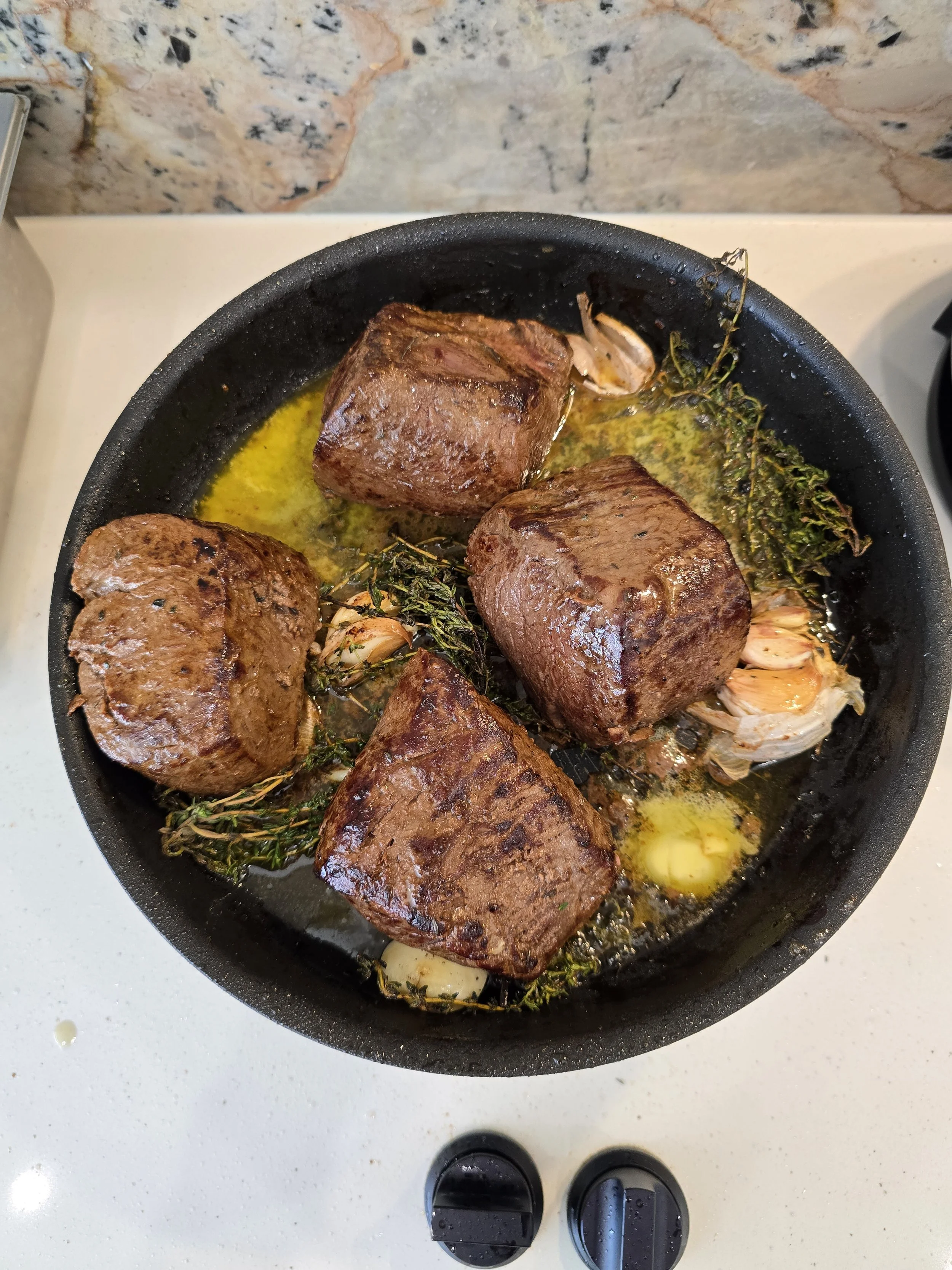 Seared steaks with garlic and herbs in a pan