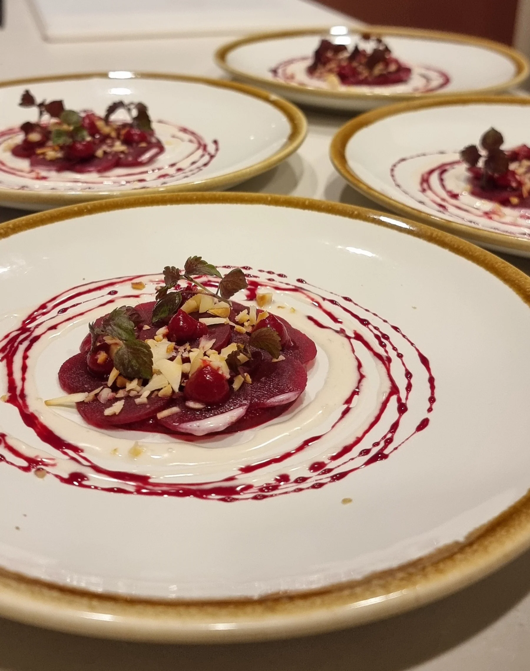 Four plates of gourmet beetroot salad with local macadamia, garnished with herbs.