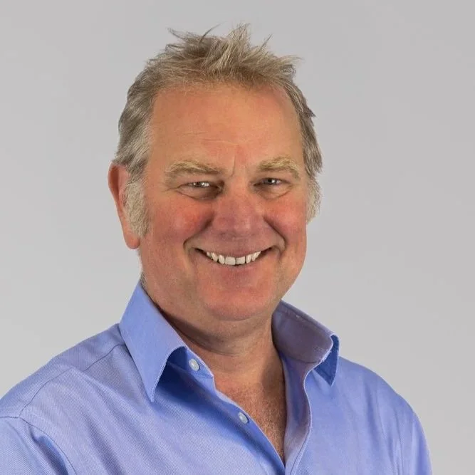 A smiling man with short, tousled hair outdoors in black and white.