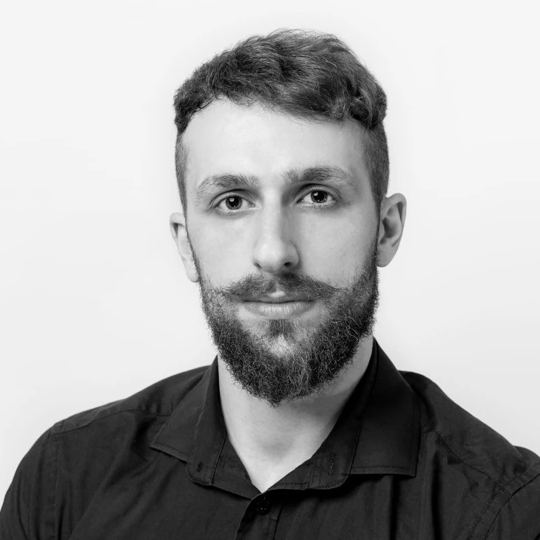 Black and white portrait of a man with short hair, beard, and mustache, wearing a dark collared shirt, facing forward against a plain background.
