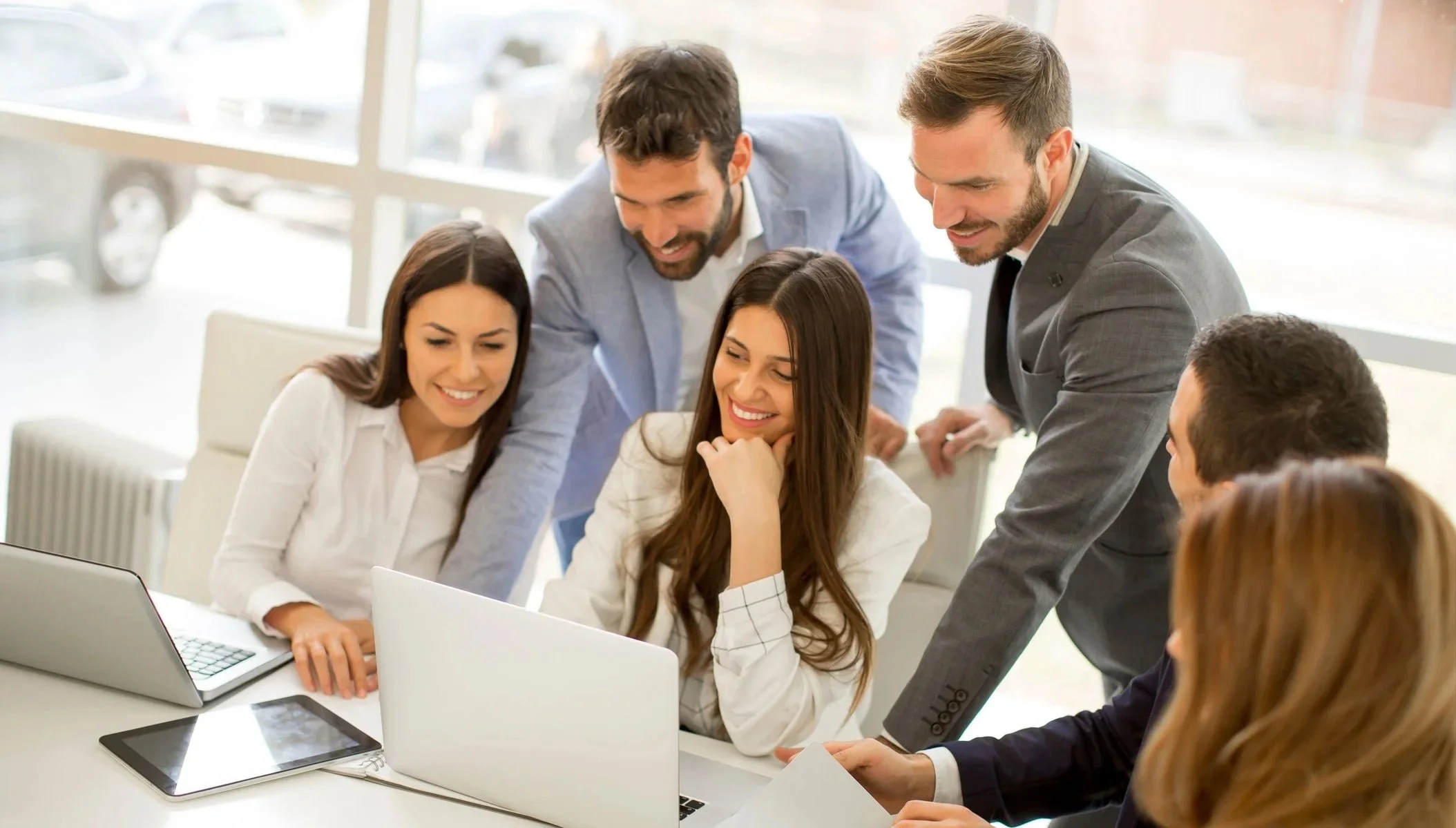 Gruppe mennesker i et kontor, alle ser på en laptop og smiler, to menn står og peker på skjermen.