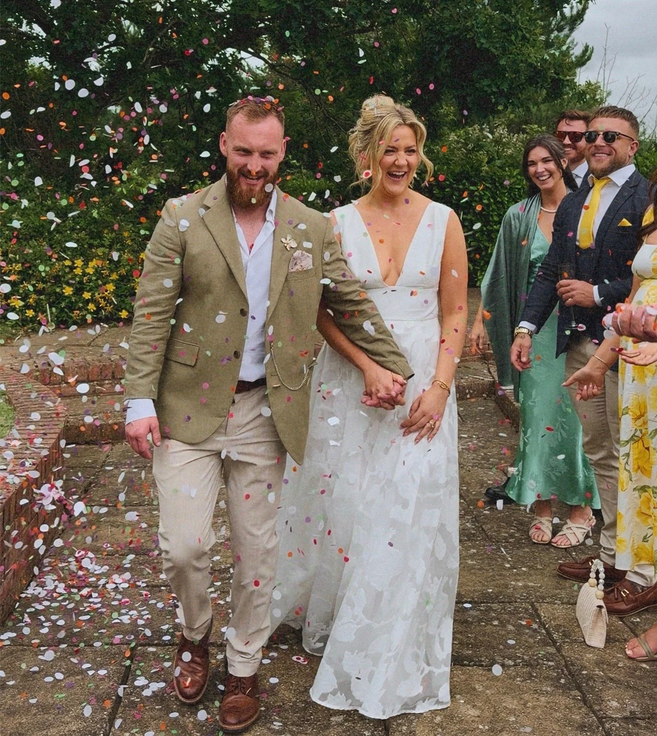 Couple holding hands and walking through falling confetti during their wedding ceremony, surrounded by happy guests. Dudley wedding content creator.