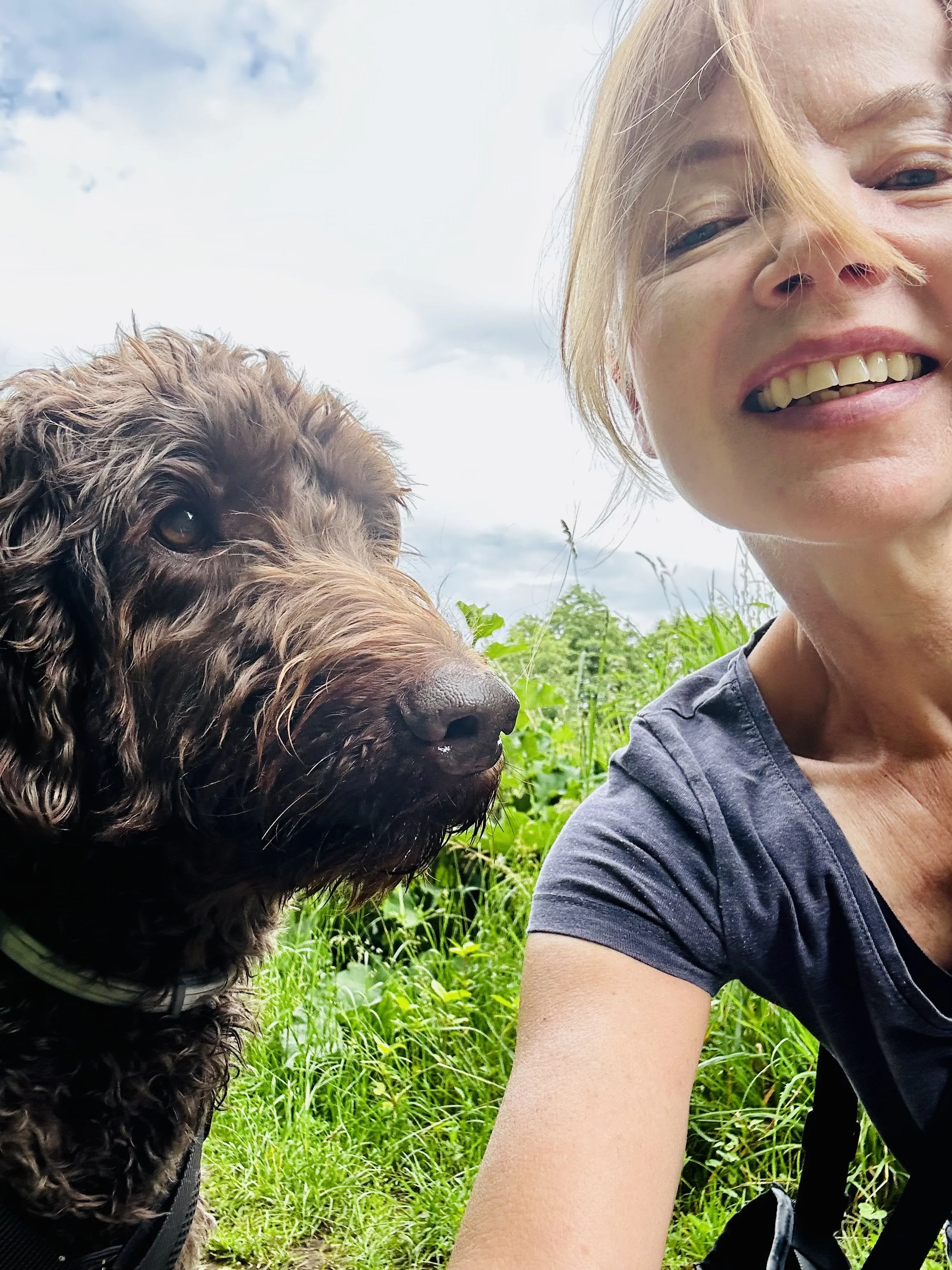 Beziehungsaufbau: Frau macht einen Selfie mit ihrem Hund im Freiengrüner Hintergrund bei bewölktem Himmel