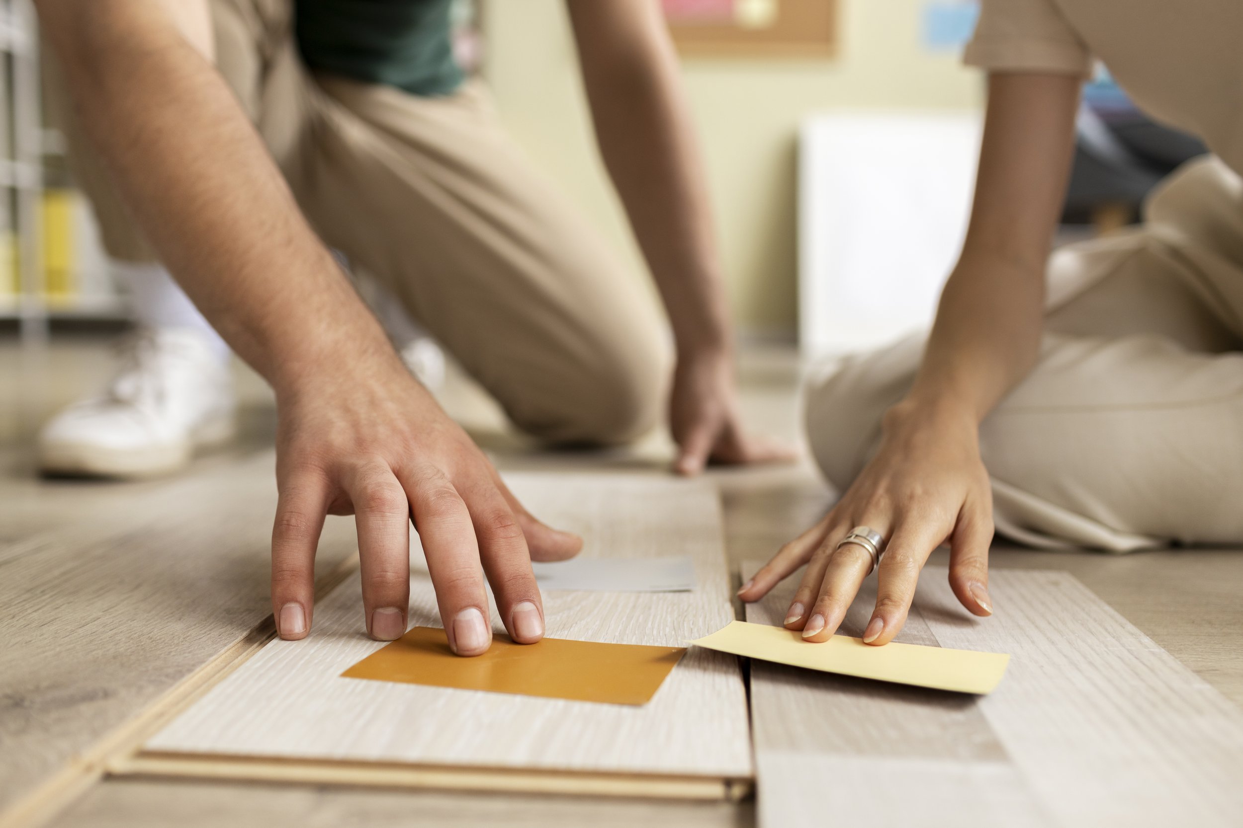 Two people kneeling on the floor, working on a woodworking project with wood and paint swatches.