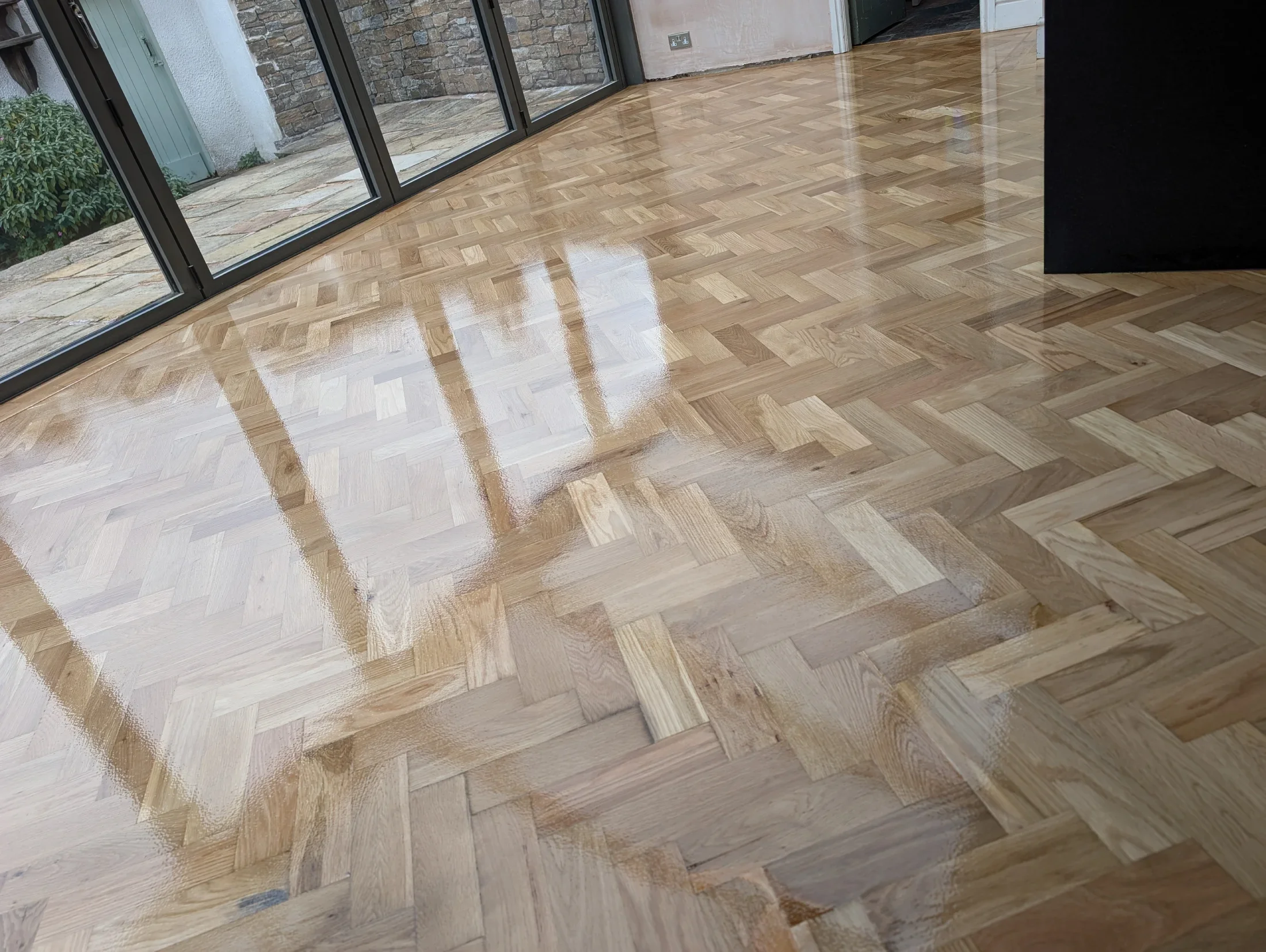 A room with a polished wooden herringbone parquet floor, glass sliding doors, and outside patio view.