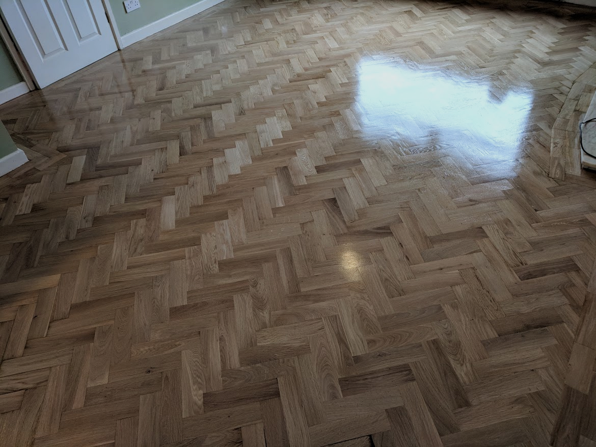 Polished wooden parquet floor with a herringbone pattern in a room with a white door and light green walls.