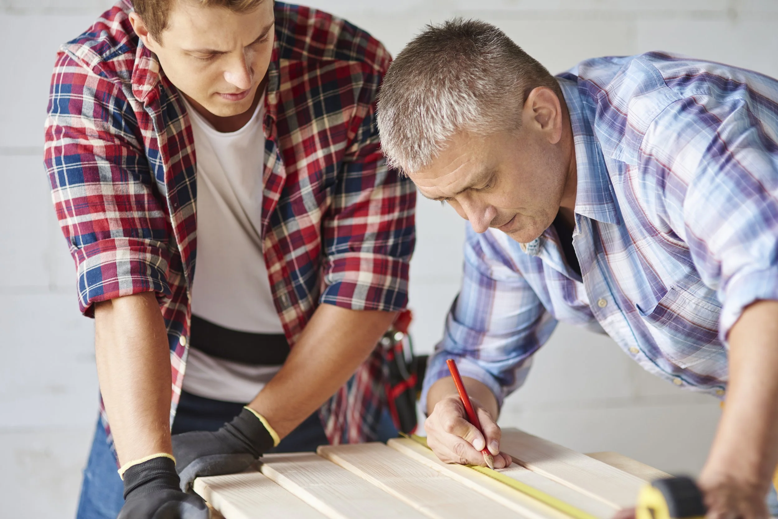 Two men working together on a woodworking project, measuring and marking a piece of wood.