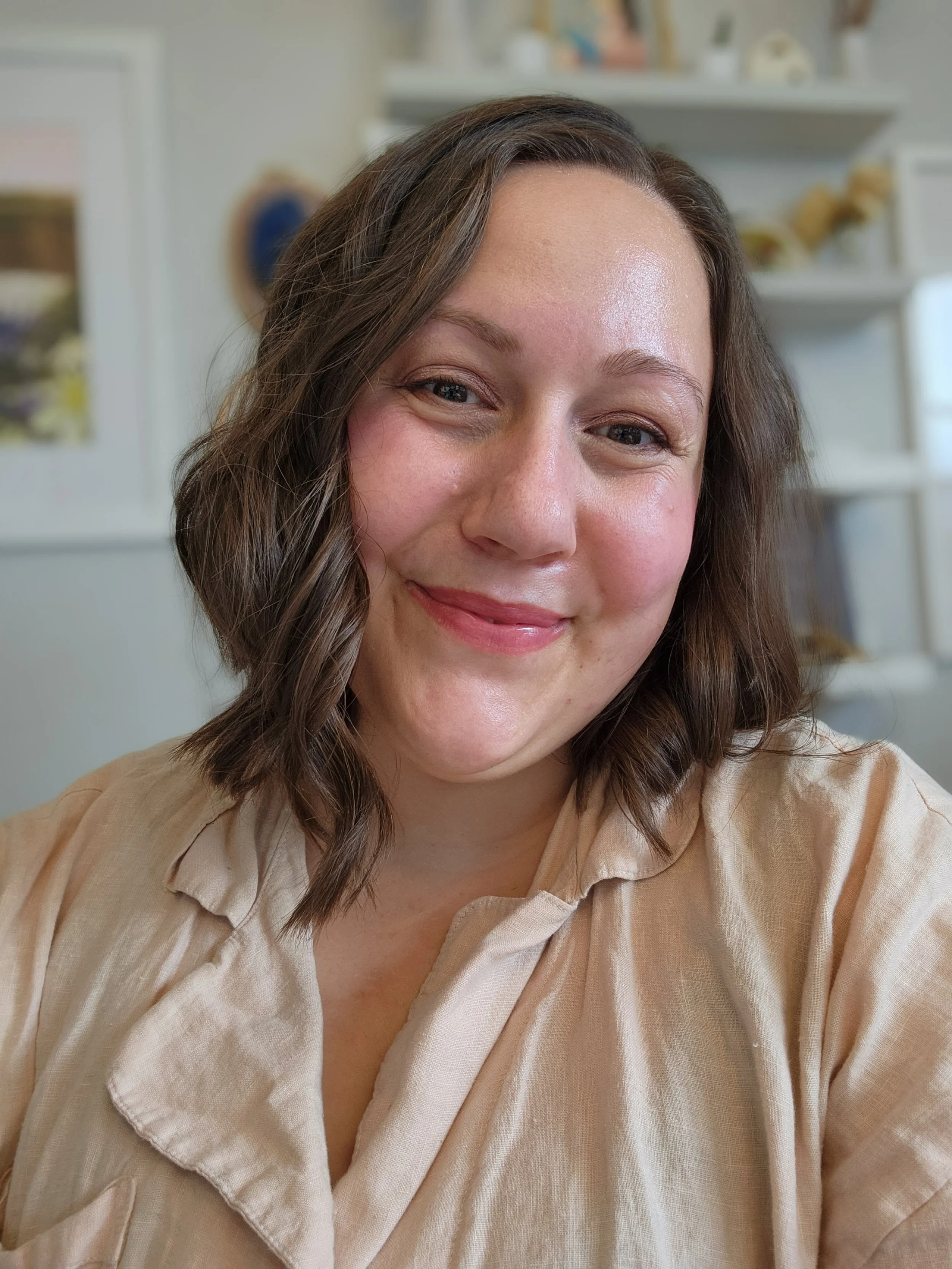 A young white woman in her 30's smiles at the camera. She has brown hair and wears a light pink dress shirt.