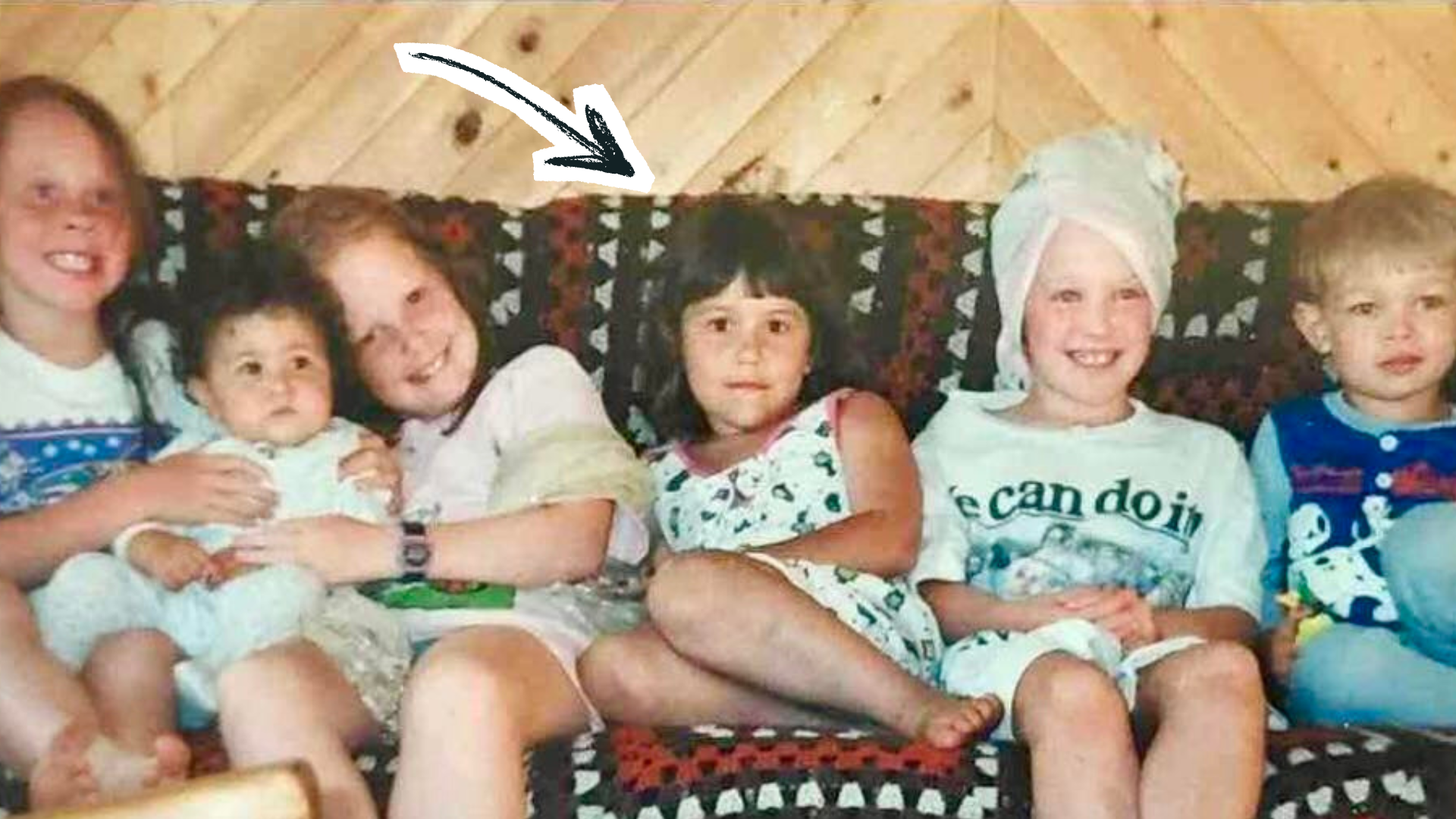An old childhood photo, with 6 children of different ages seated on a sofa. A graphic of an arrow points to the child in the middle the point out the author.