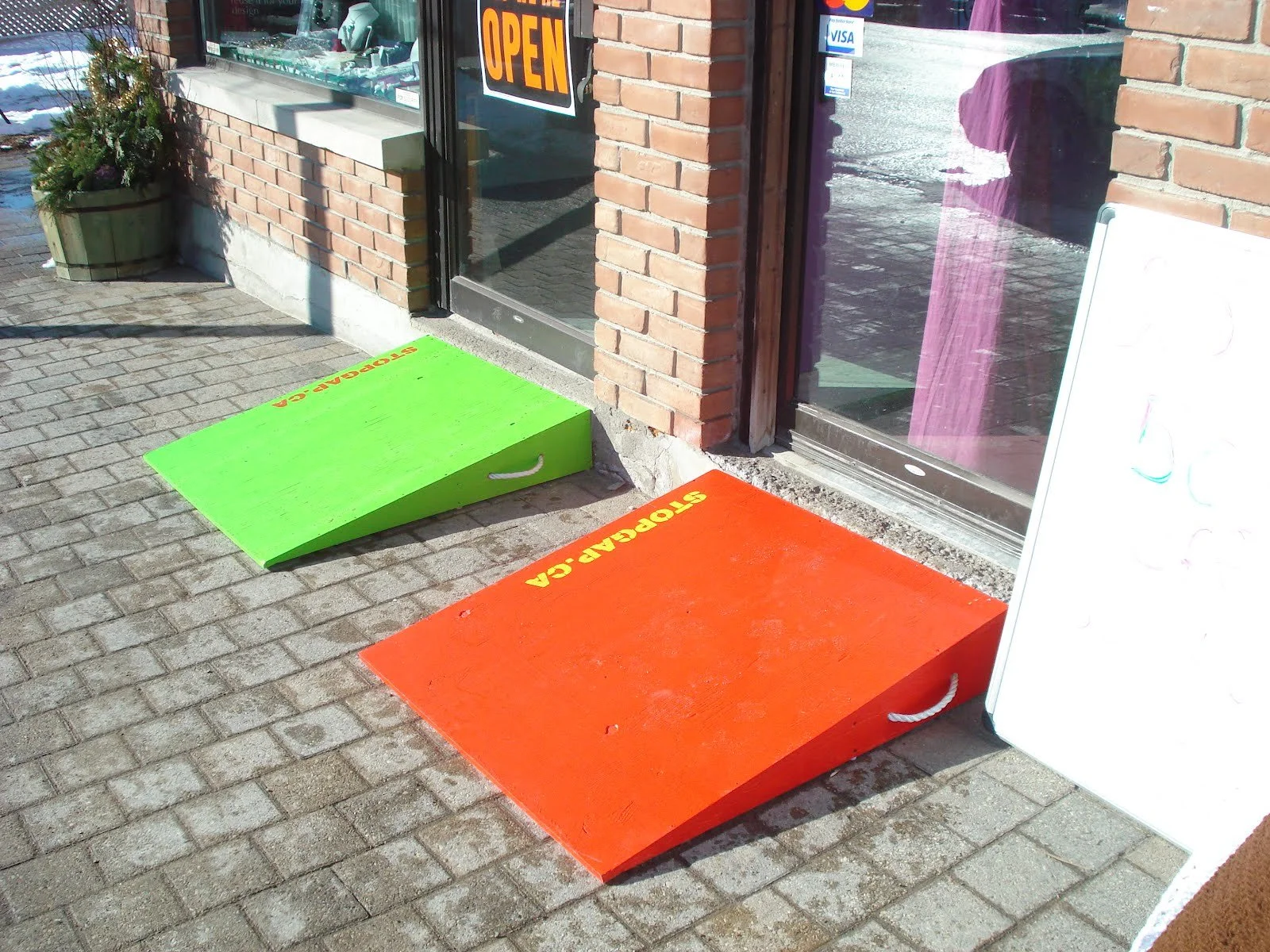 Two colourful portable ramps sit on the cobblestone in front of two shop entrances in Stouffville, Ontario, as part of StopGap Canada's accessibility initiative.