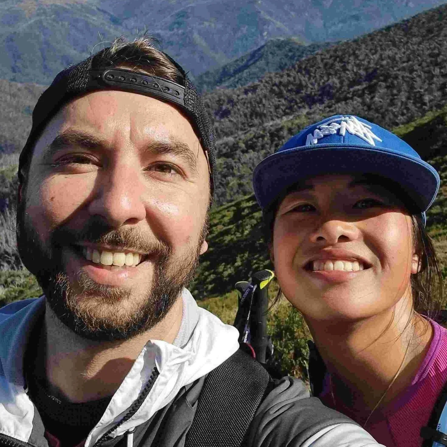 Smiling Hike Tribe's clients taking a selfie outdoors with a mountainous landscape in the background.