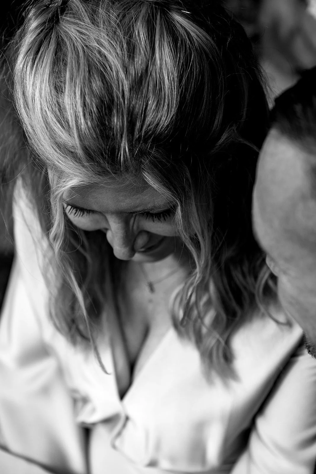 Black and white close-up of a woman looking down, with wavy hair and a gentle expression, wearing a light-colored blouse.