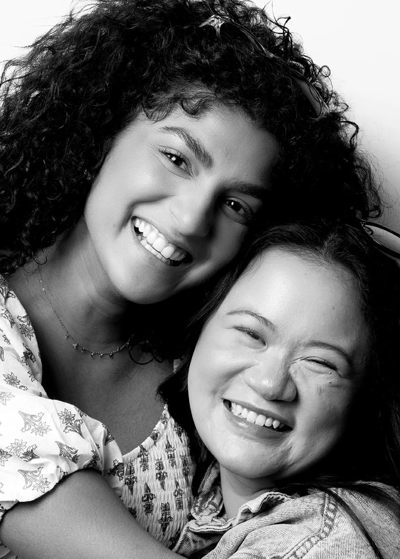 Two women smiling and hugging each other in black and white.