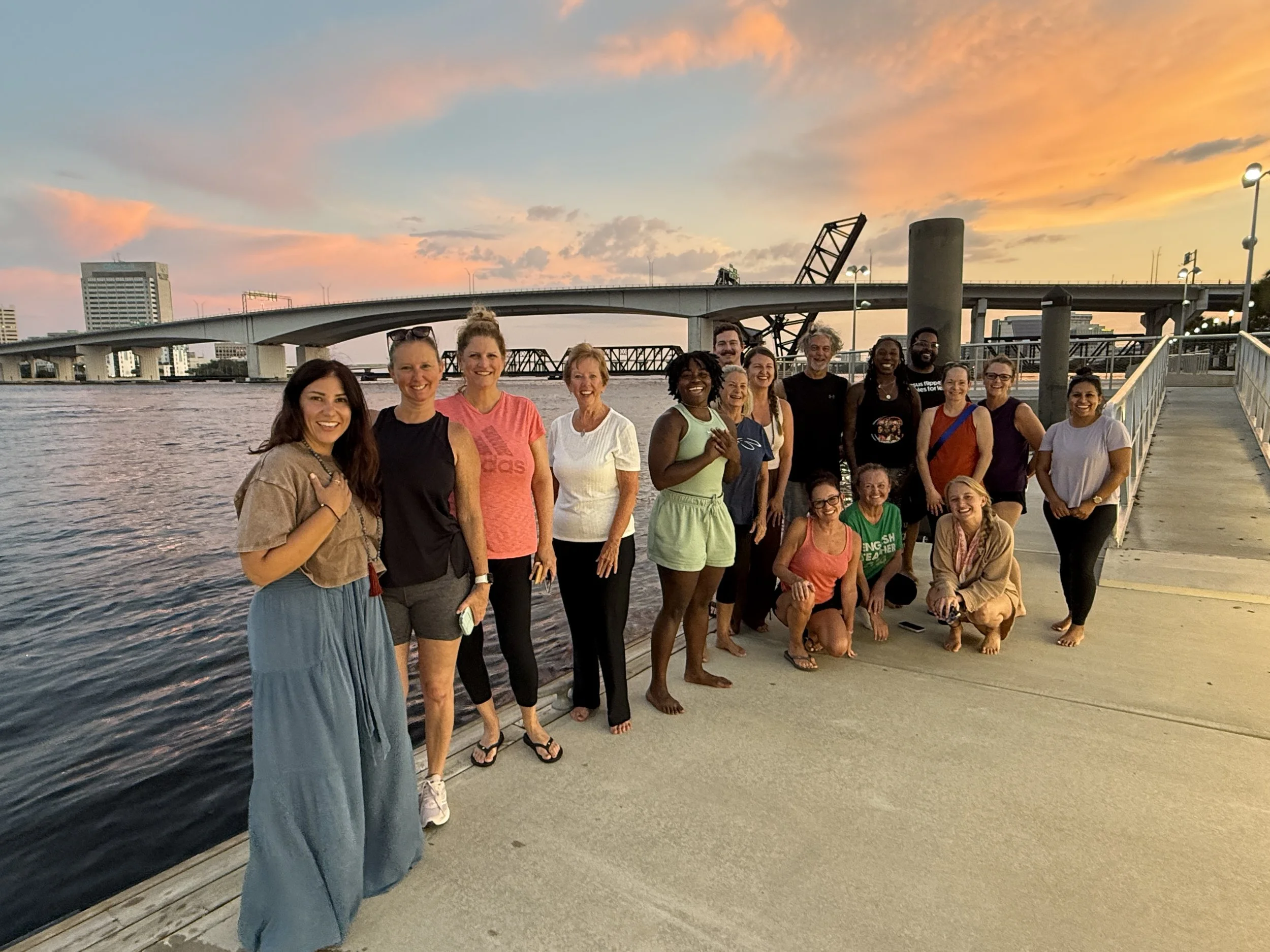 Group standing in dock in front of river and bridge at sunset