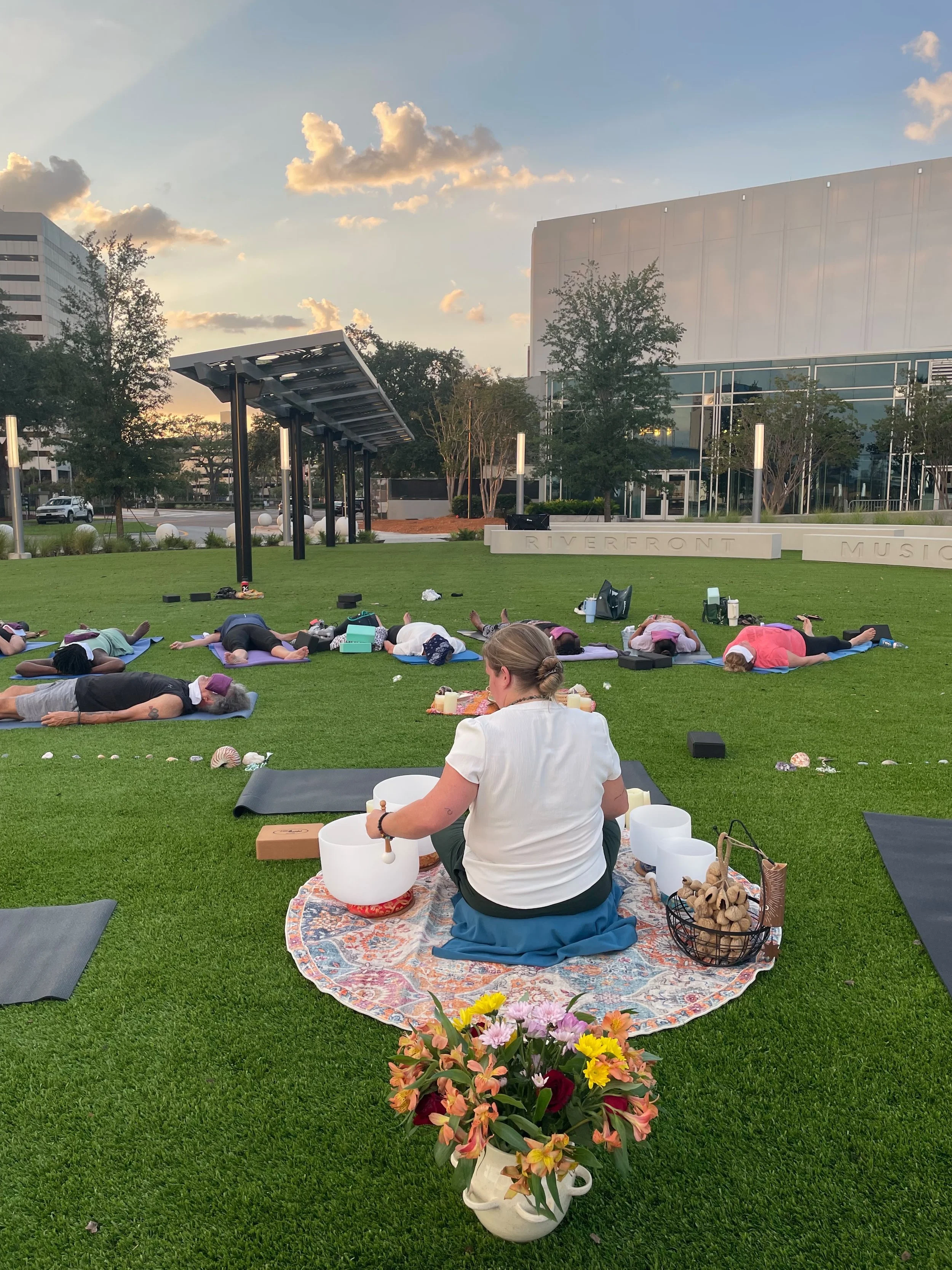 Woman playing singing bowls while students are laying on mats in front of her on the grass