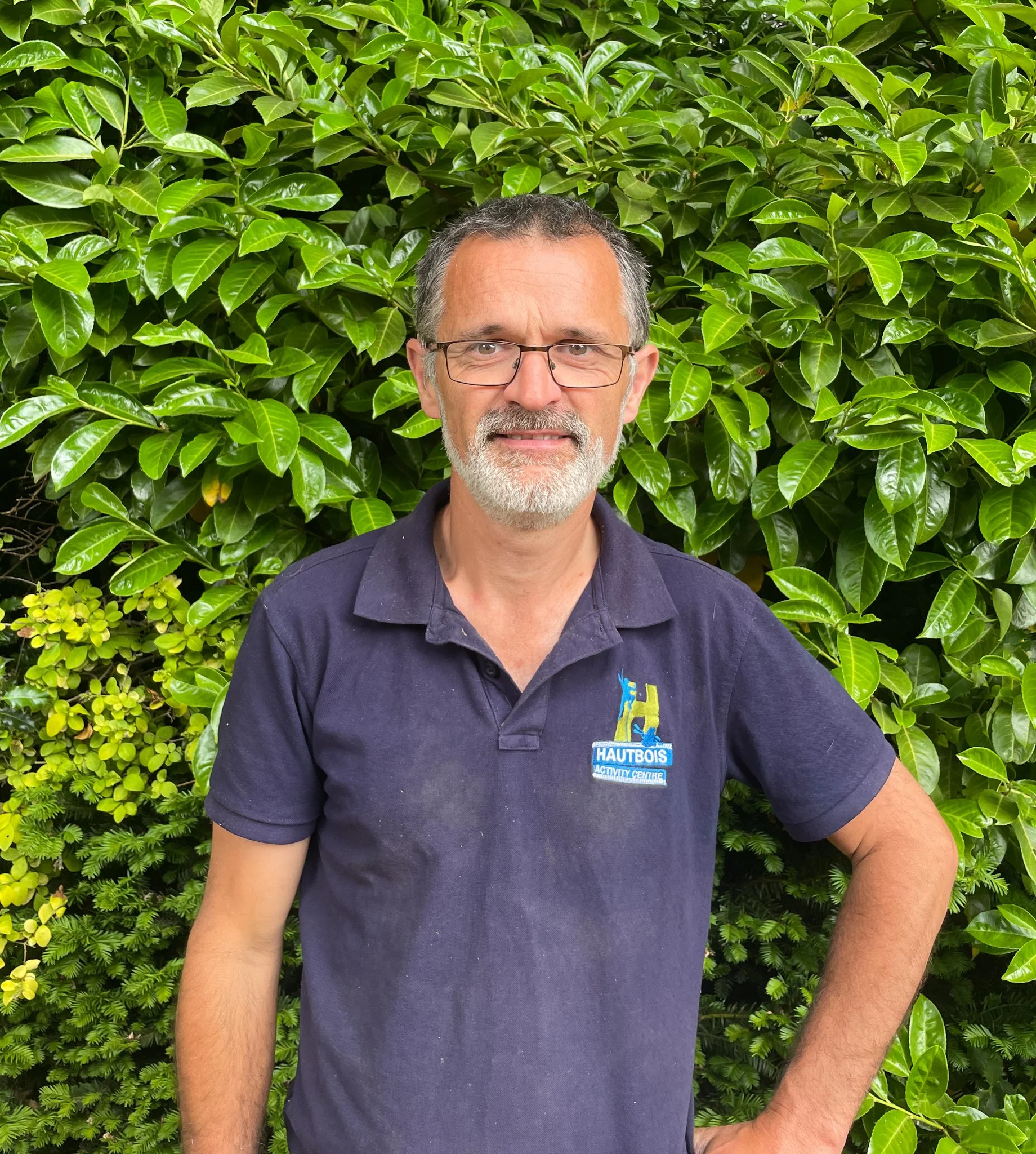 A man wearing a blue chef's coat standing in front of a green bush.