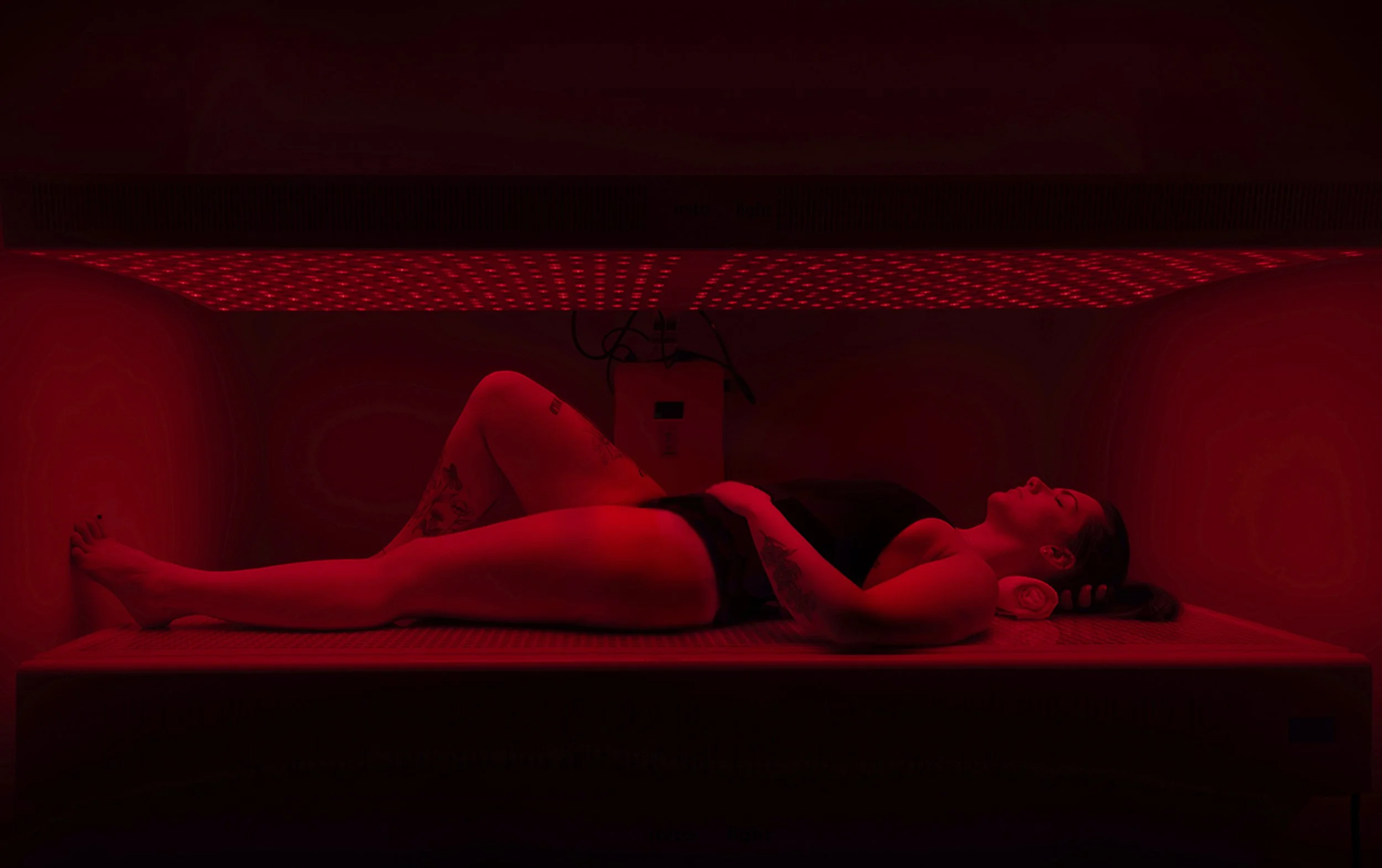 A woman lying inside a red light bed, with her eyes closed and relaxing.