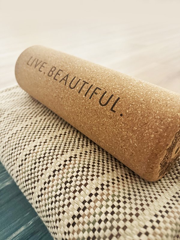 A cork roller with the words "Live, Beautiful" engraved on it, resting on a textured fabric surface.