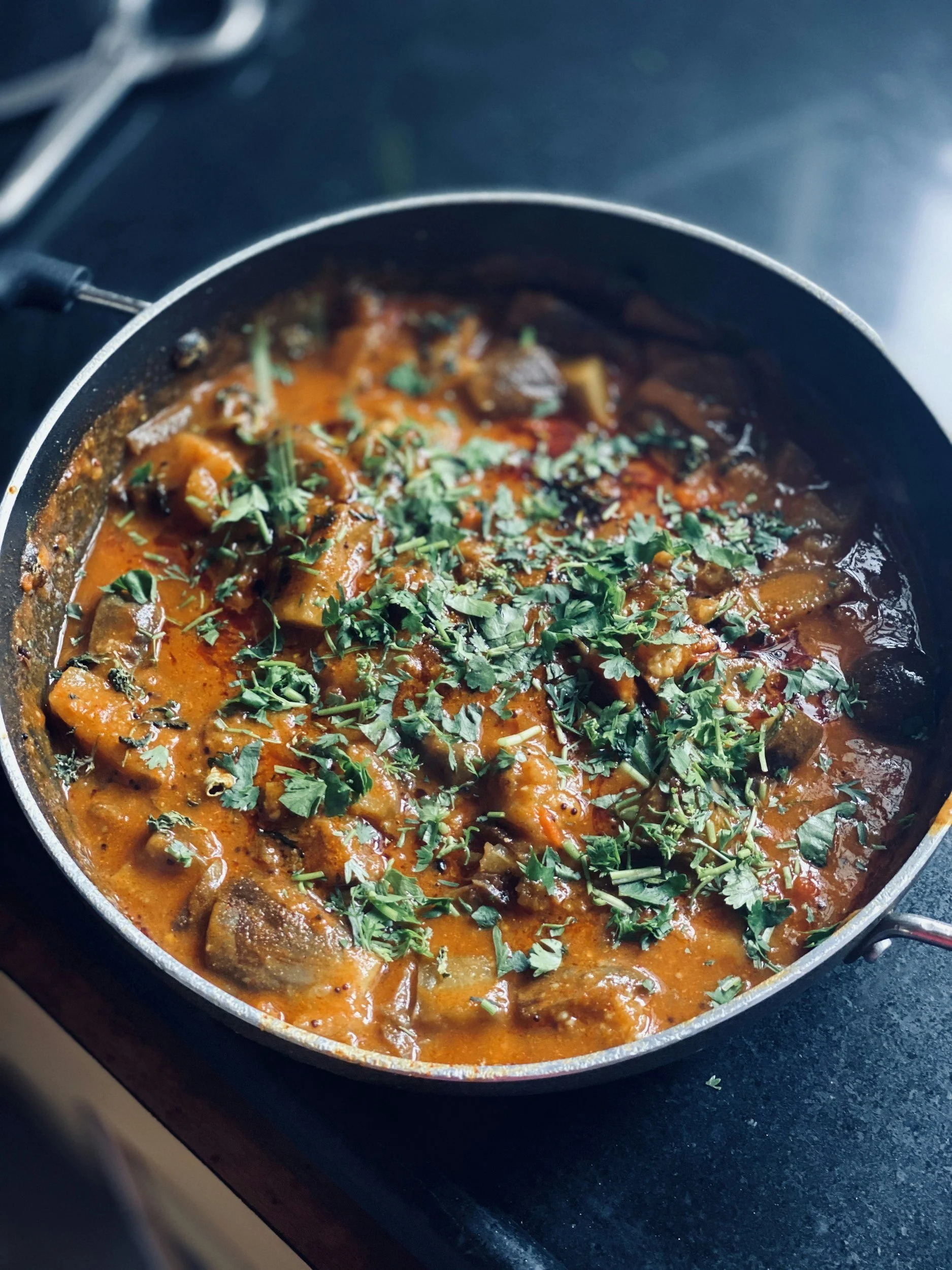 A pan of beef stew garnished with chopped cilantro on a dark countertop.