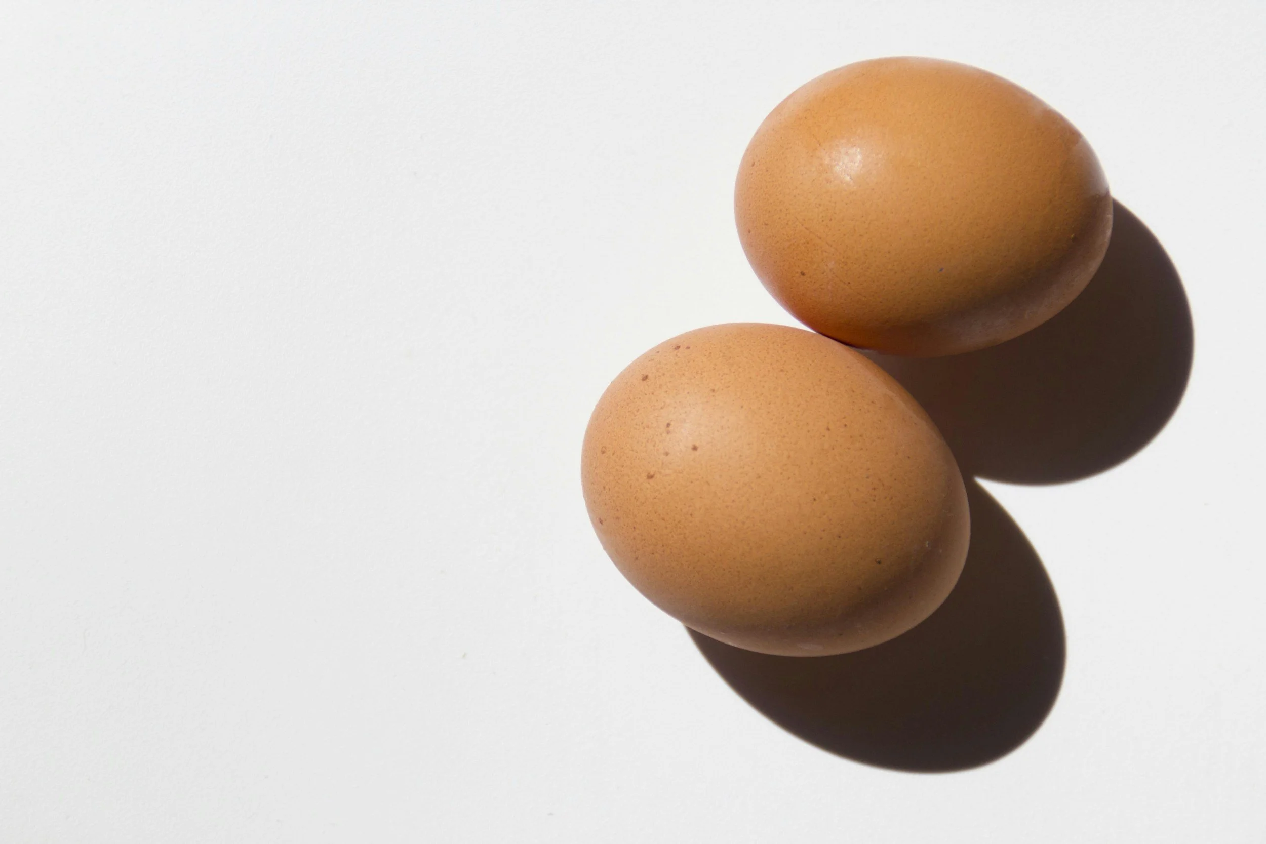 Two brown chicken eggs on a white surface, casting shadows.