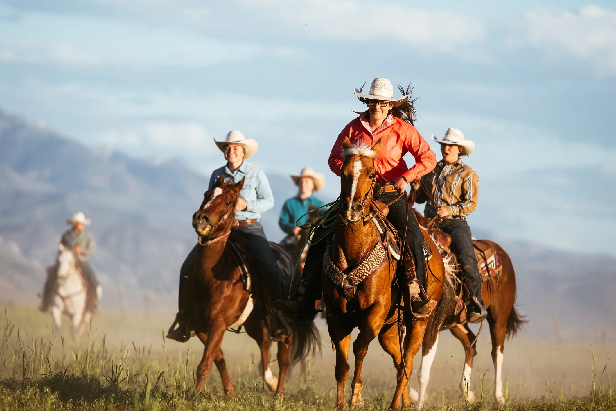 A group of riders wearing cowboy hats riding horses through an open field.