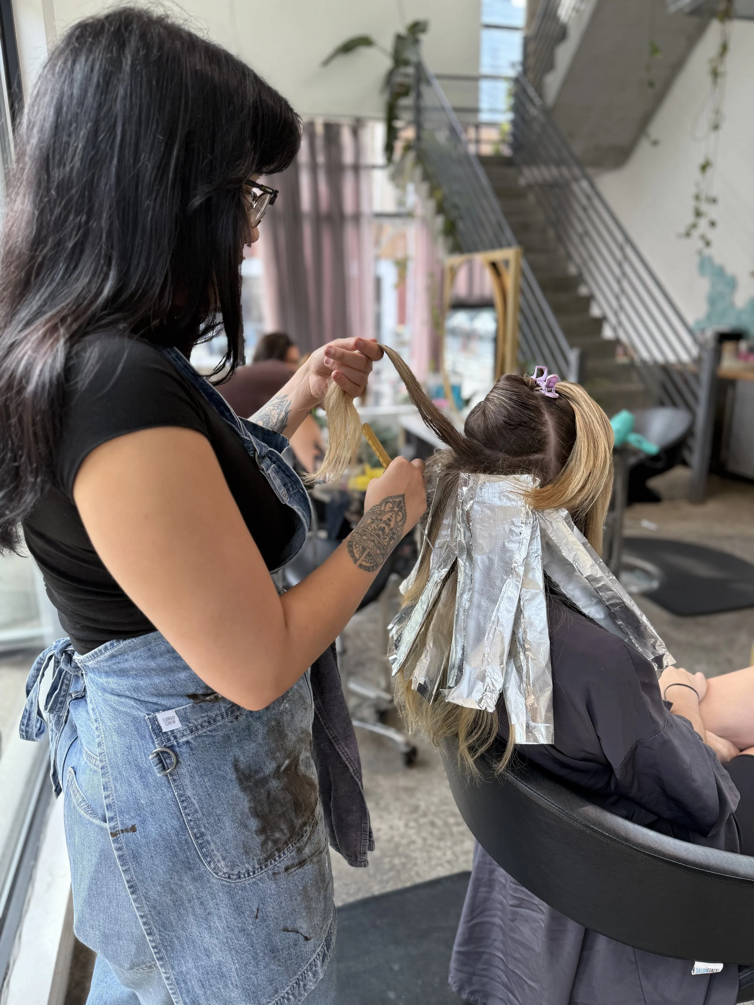 Gem House Salon colorist applying customized foil highlights to create dimensional blonde hair in Brooklyn.