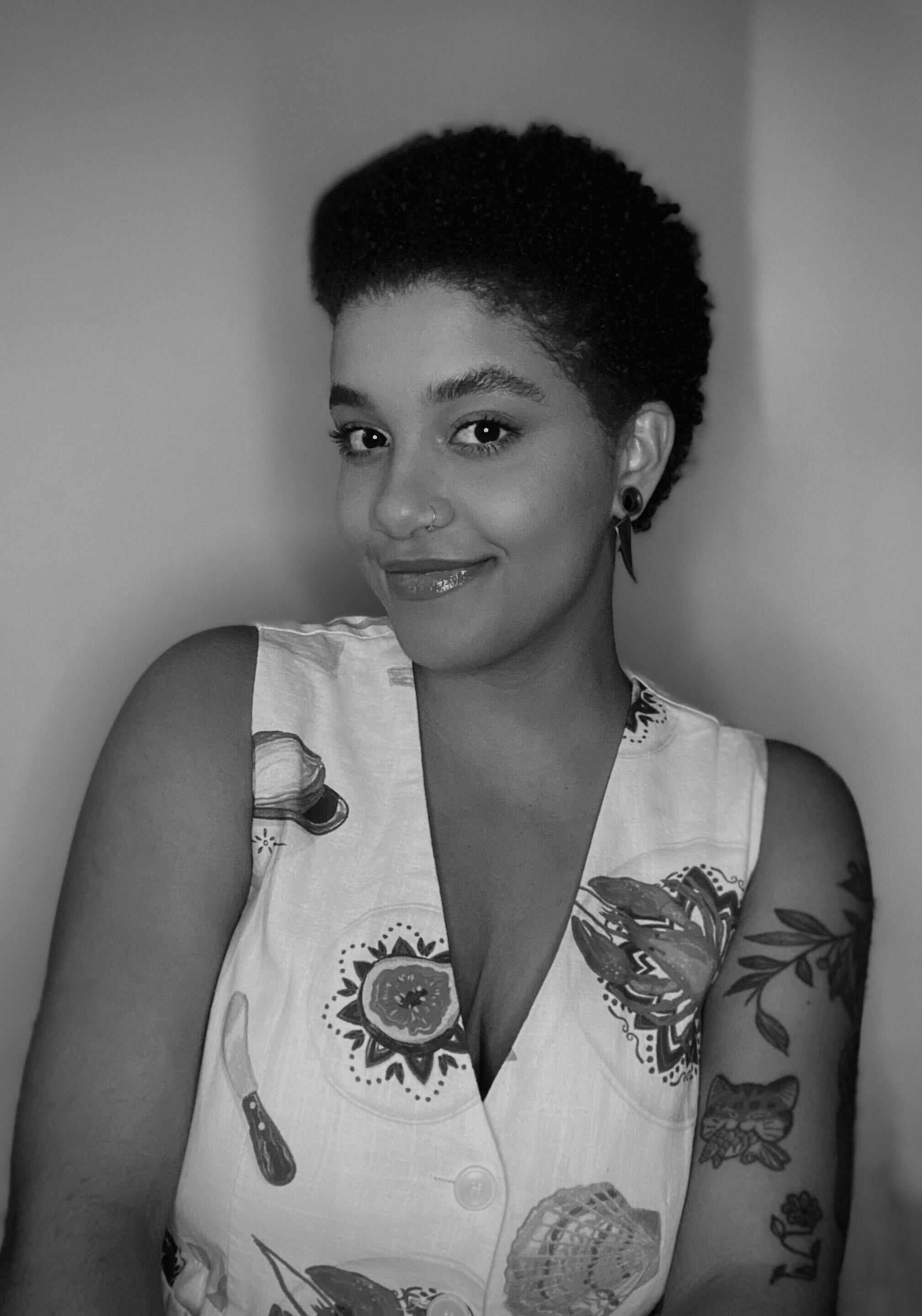 Curly hair specialist and haircutting stylist at Gem House Salon in Greenpoint, Brooklyn, specializing in curly haircuts, natural and textured cuts, bobs, and all haircut services, smiling with short curly hair and a nose piercing.